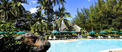 A poolside area with lounge chairs and umbrellas, surrounded by palm trees and a clear blue sky.