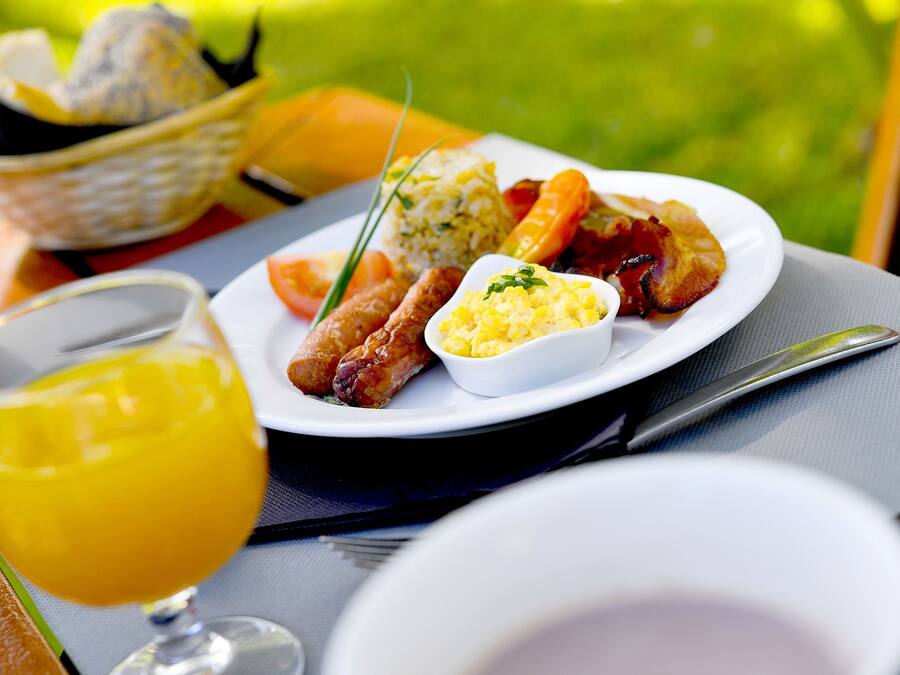 Prato de café da manhã com ovos, bacon, salsicha e torradas, acompanhado de um copo de suco de laranja.