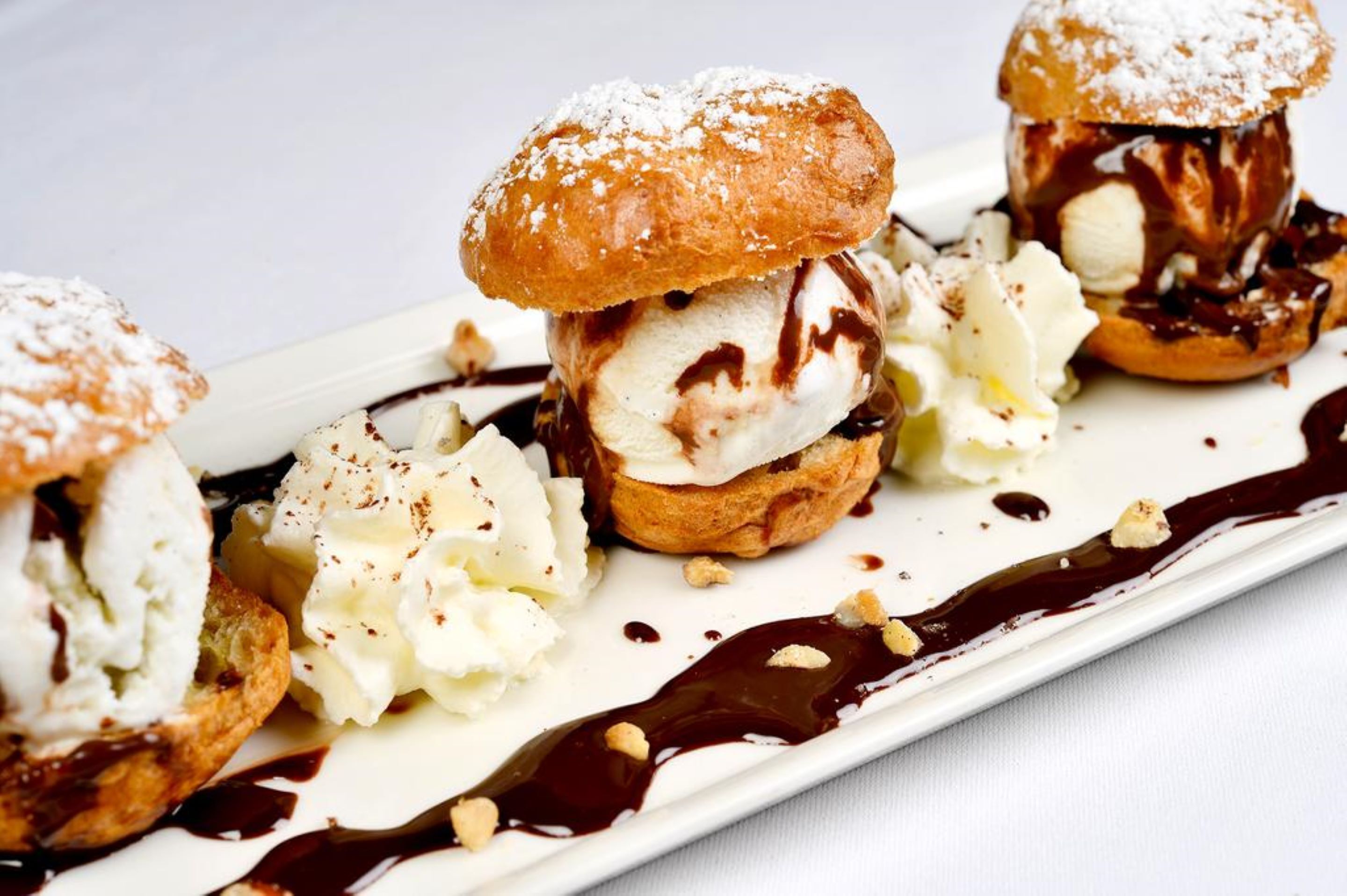 Three dessert items, likely ice cream sandwiches, on a white plate with chocolate sauce and powdered sugar.