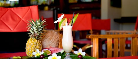 Een tafel met een ananas, kokosnoot en een drankje versierd met fruit en bloemen, geplaatst op een zwarte placemat met een rode tafelkleed.
