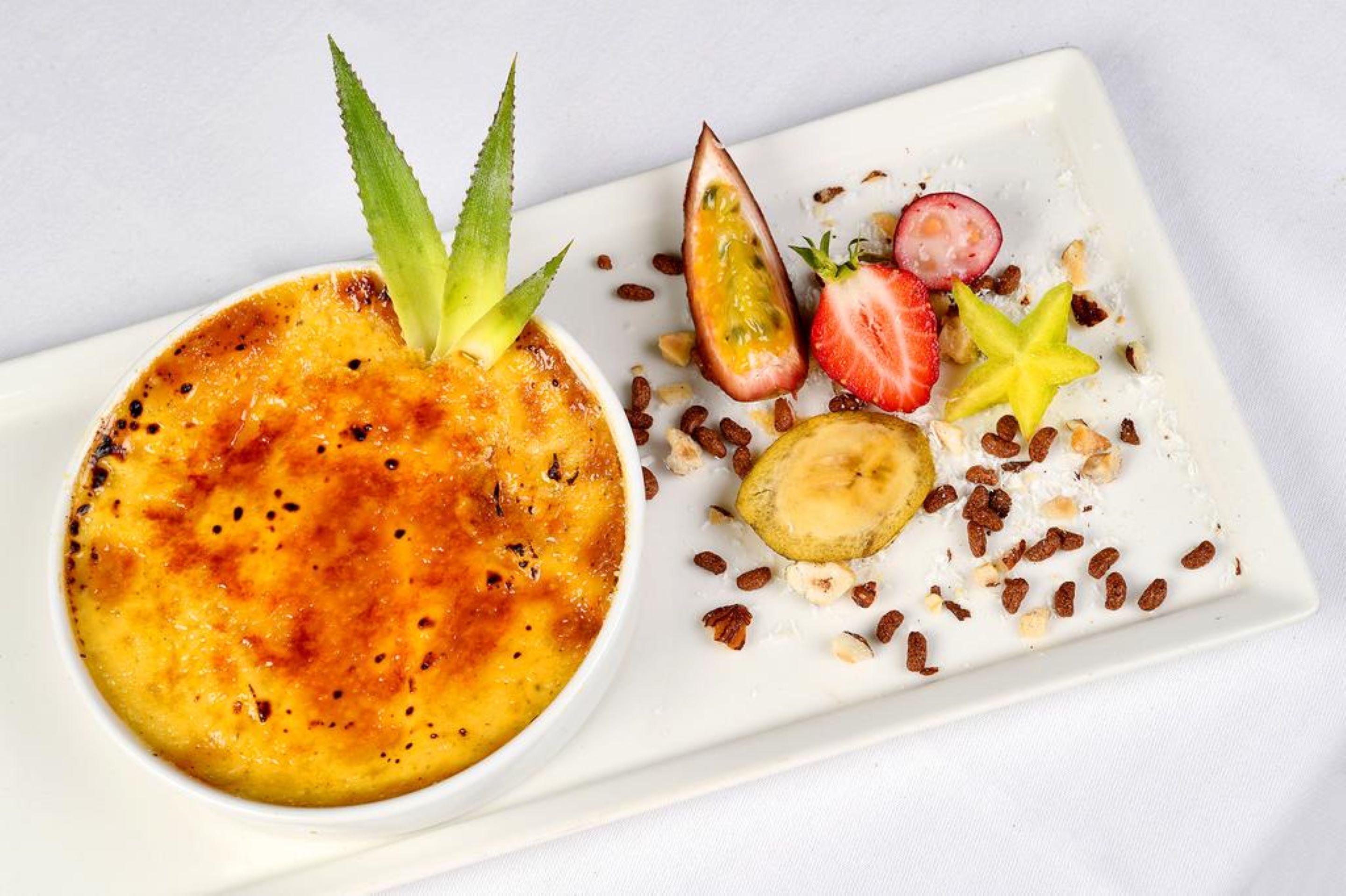 A dessert plate with a crème brûlée, strawberries, a star fruit, and nuts.