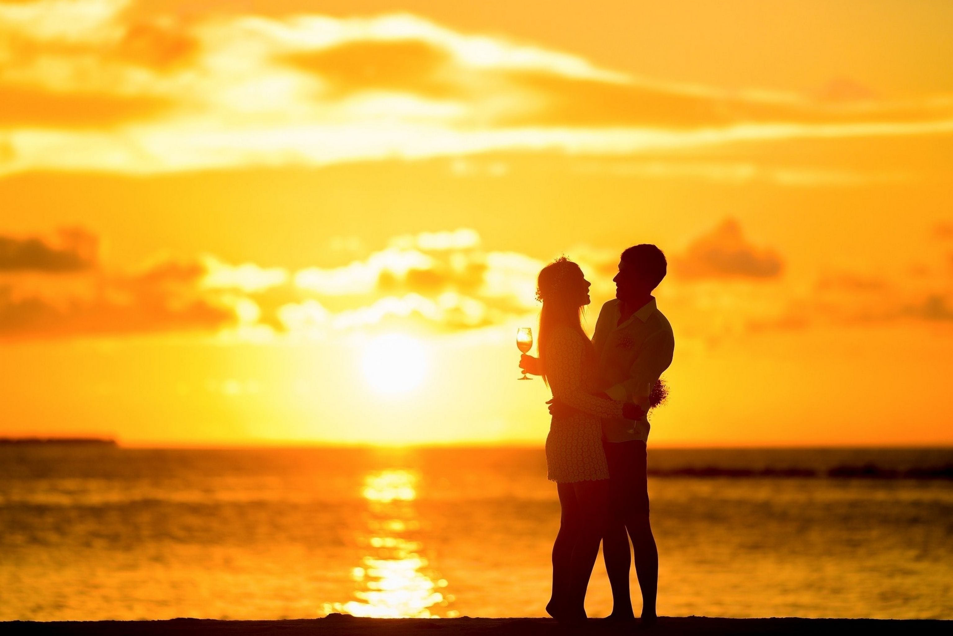 A couple standing by the sea during sunset.