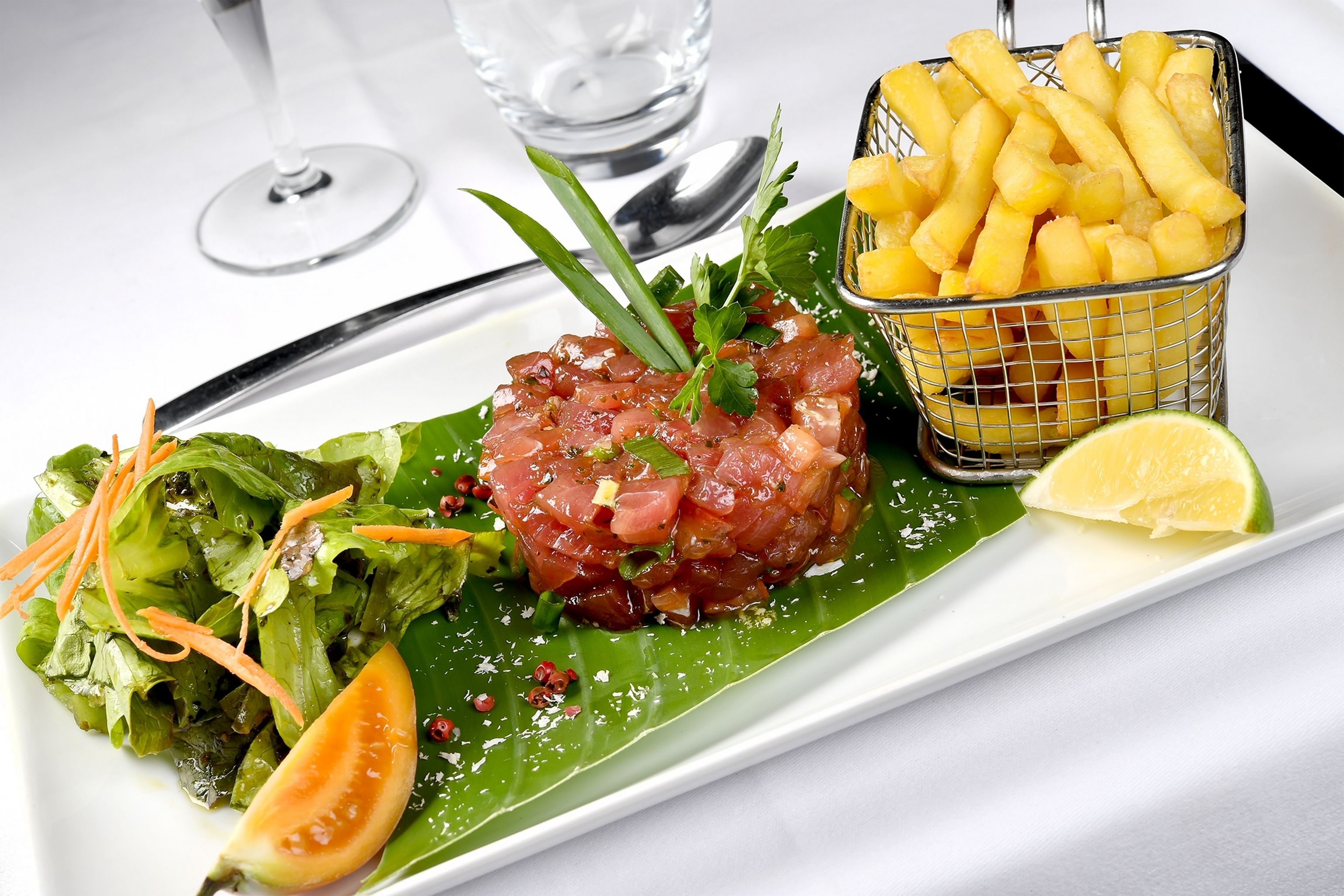 A plate with a salad, a slice of tomato, a lime wedge, and a basket of fries.