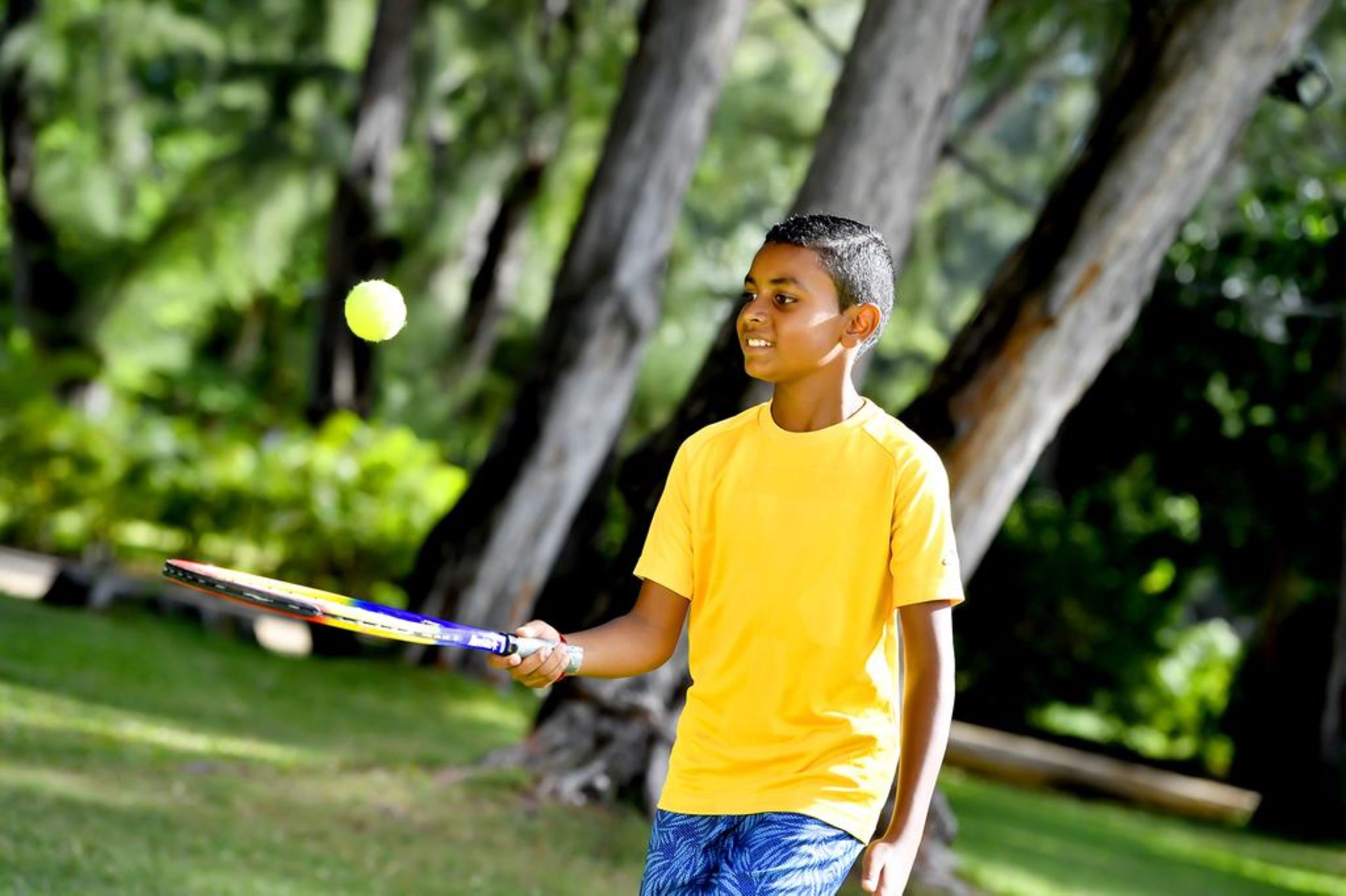 A person in a yellow shirt holding a tennis racket outdoors.