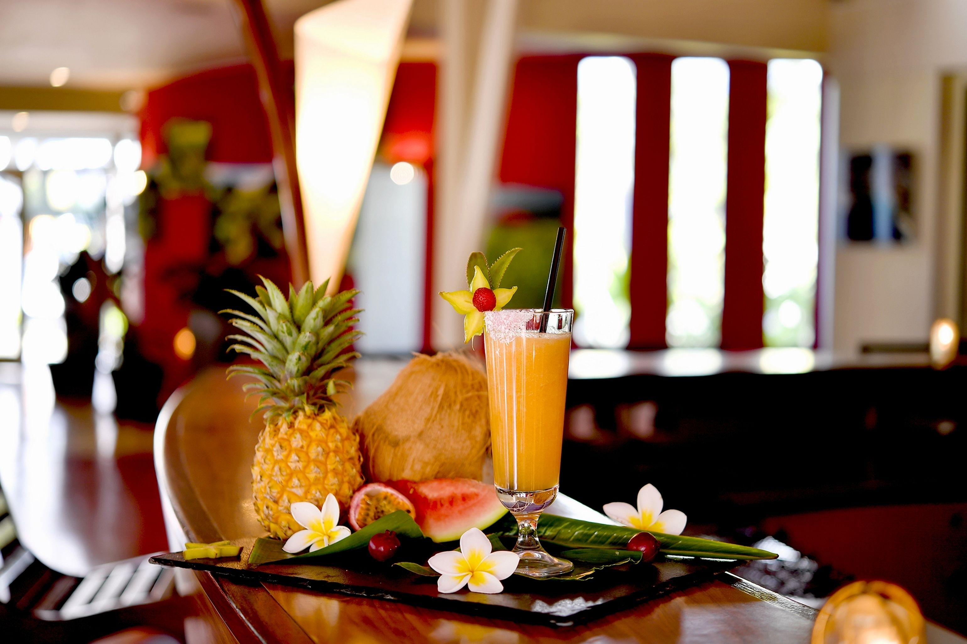 A tropical drink with a straw, pineapple, and a coconut on a table.