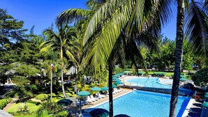 A pool area with lounge chairs and umbrellas, surrounded by palm trees and greenery. - Le Relais de L'Hermitage (Saint-Paul)