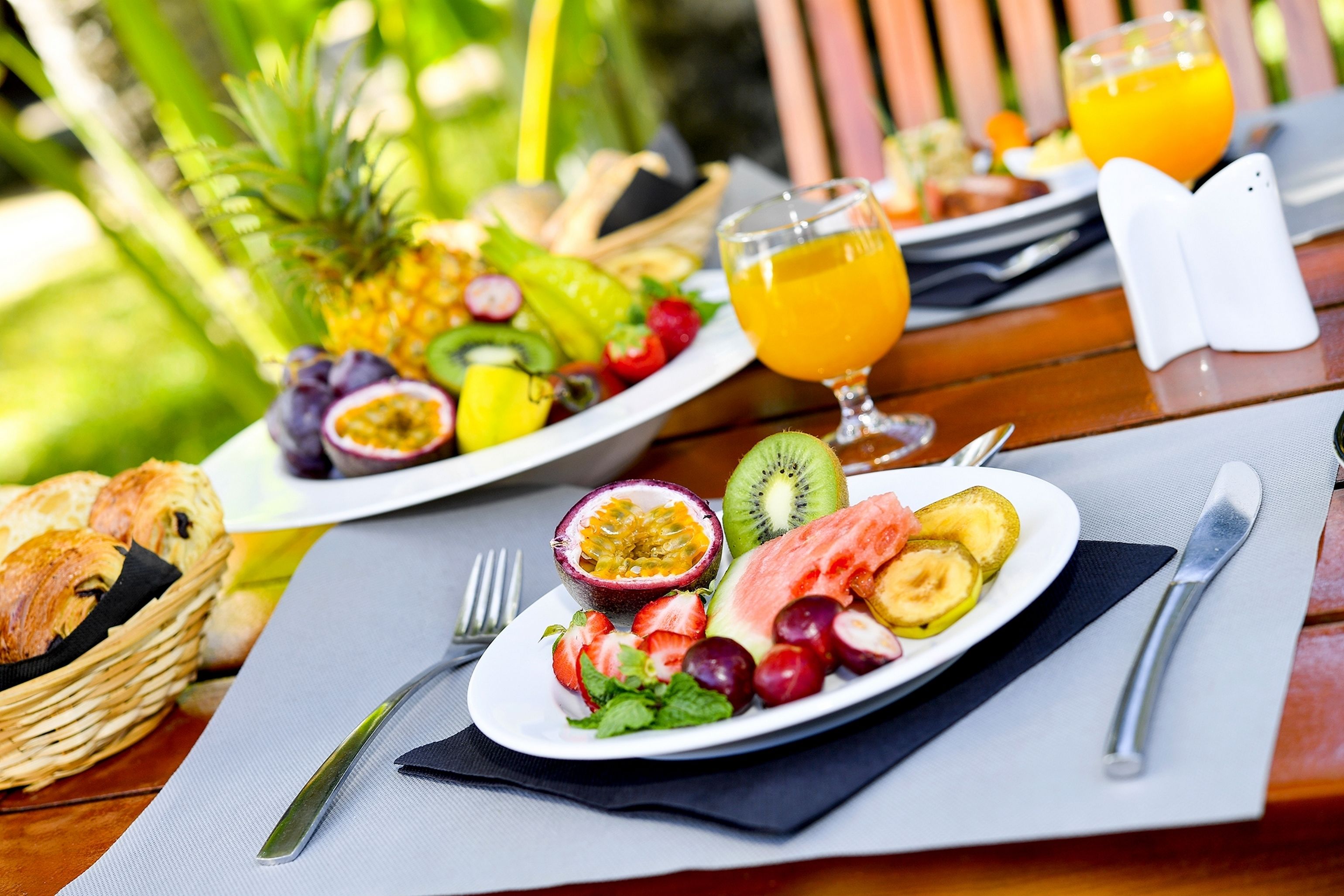 A breakfast setting with a plate of fruits and a glass of orange juice on a wooden table.