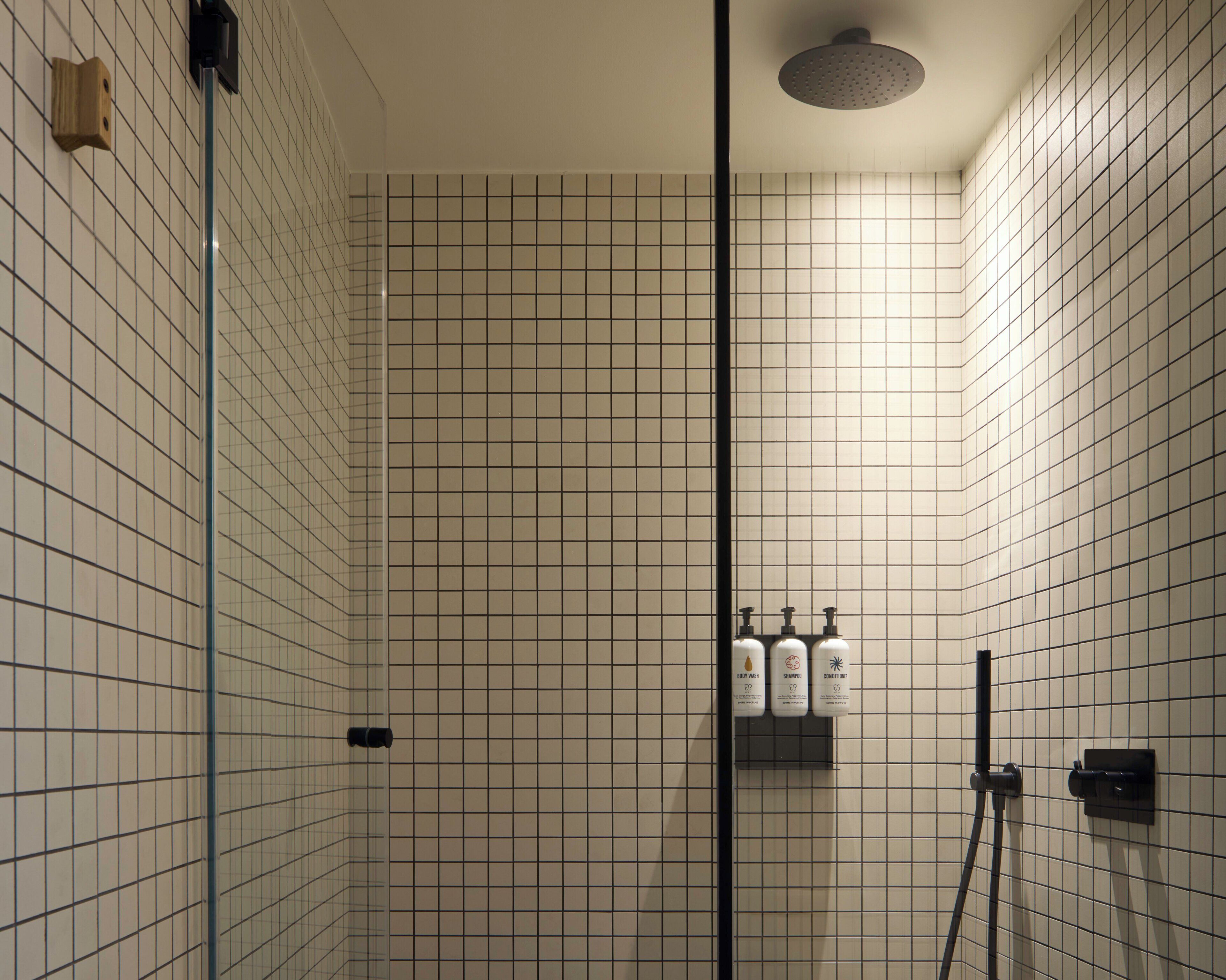 A bathroom with tiled walls, a glass shower enclosure, and three bottles of toiletries on a shelf.