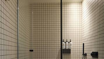 A bathroom with tiled walls, a glass shower enclosure, and three bottles of toiletries on a shelf.