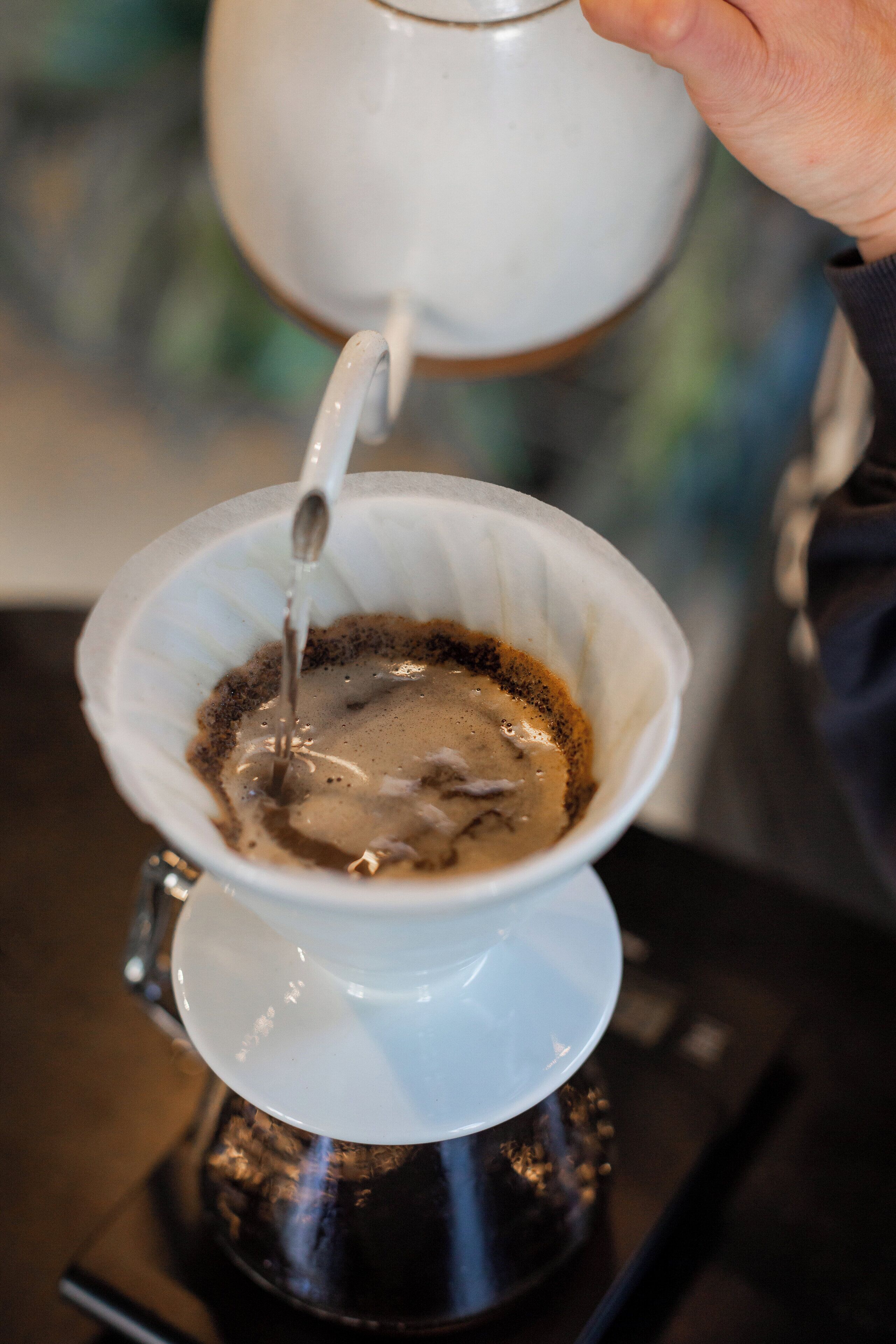 Uma mão despejando café em uma cafeteira branca.