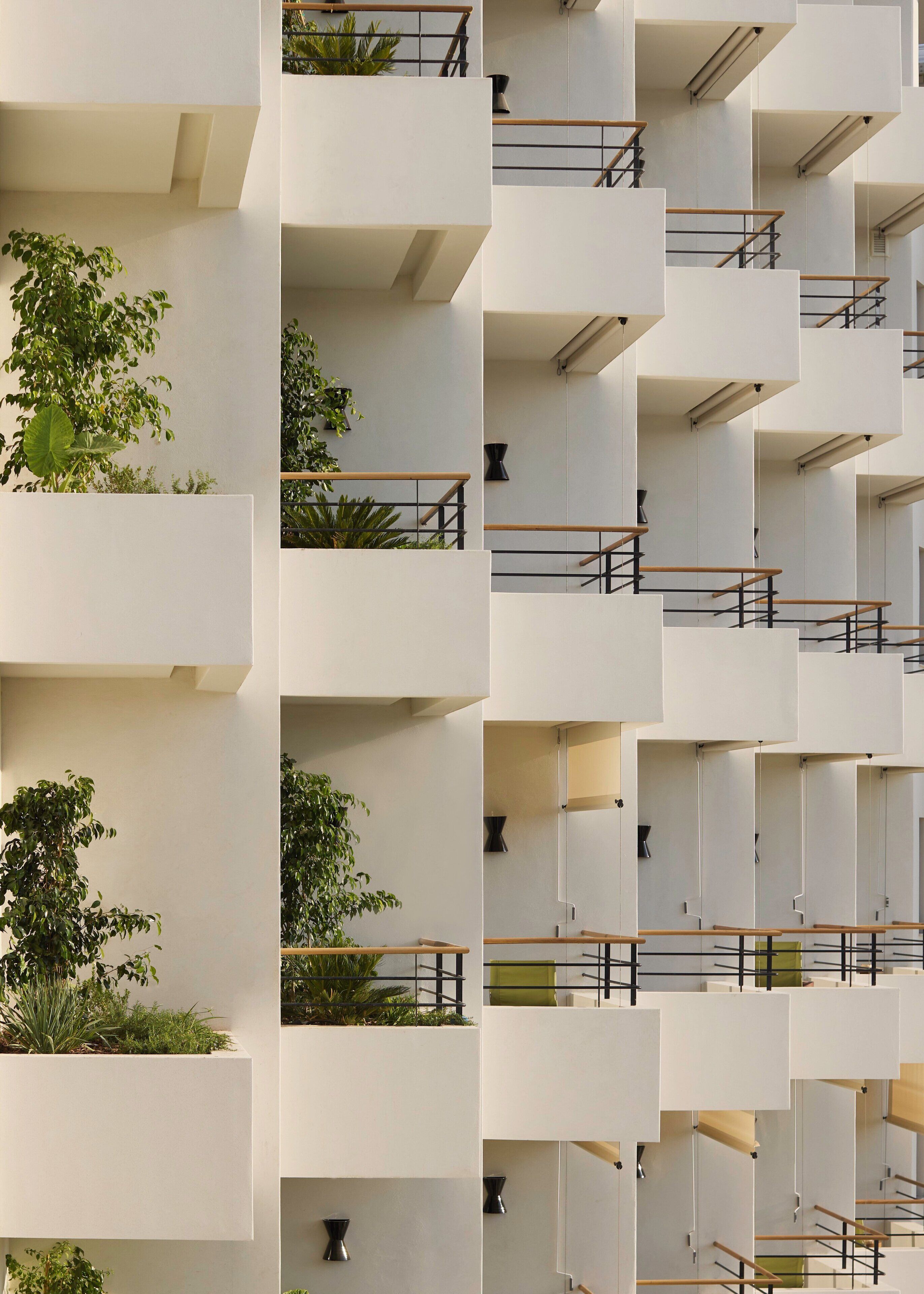 Un edificio moderno de varios pisos con balcones, algunos con plantas.