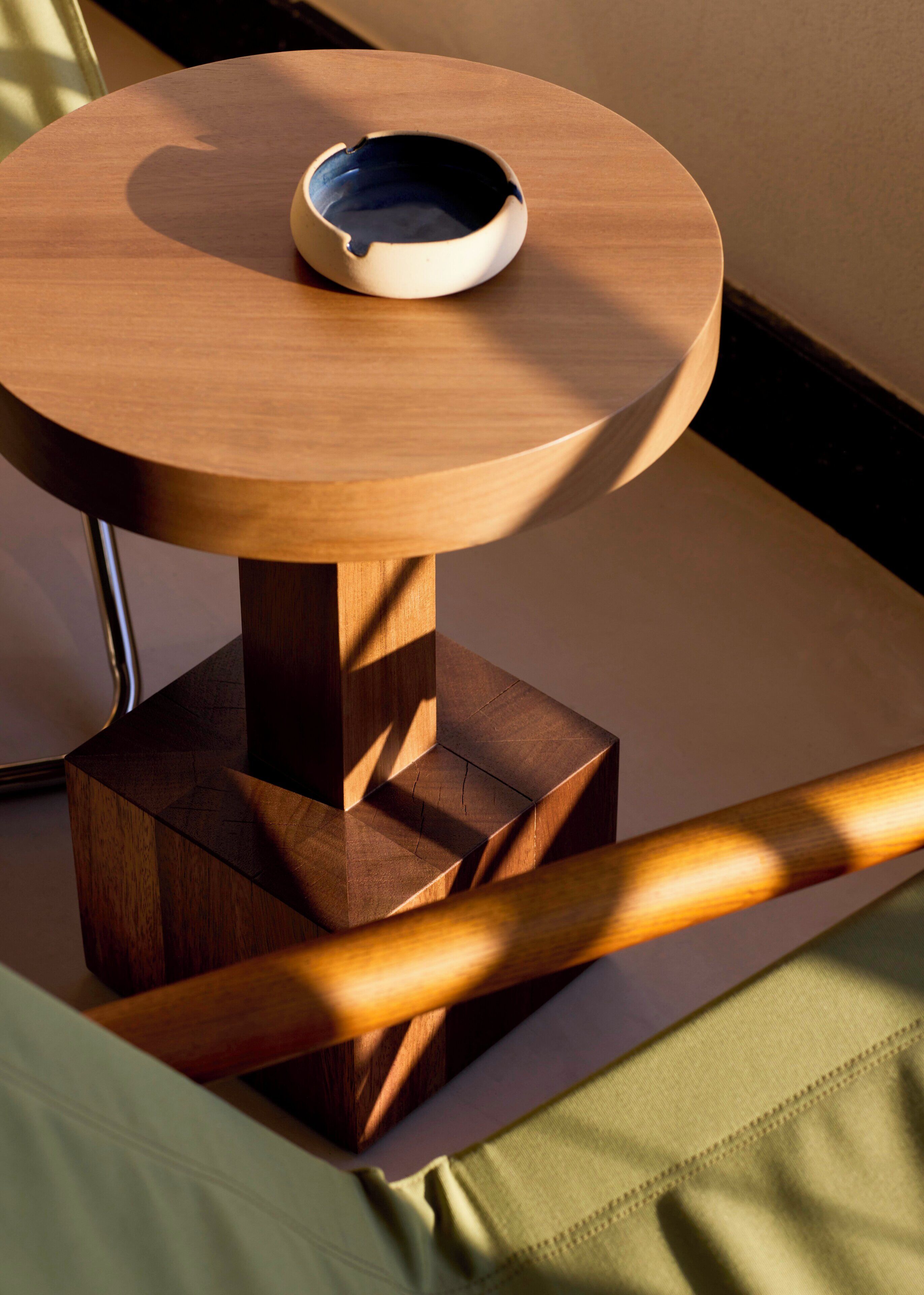 A round wooden table with a bowl on top, placed on a green fabric surface.