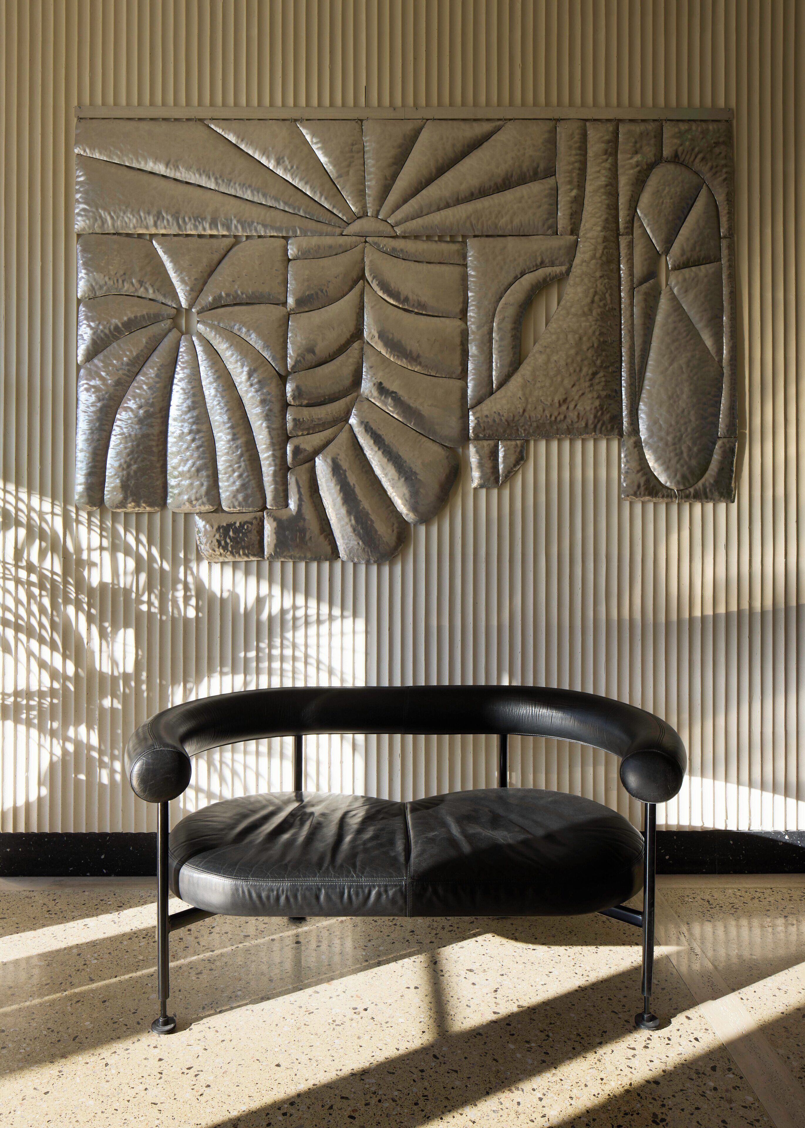 A modern room with a black leather sofa, a decorative wall panel, and a window with vertical blinds.