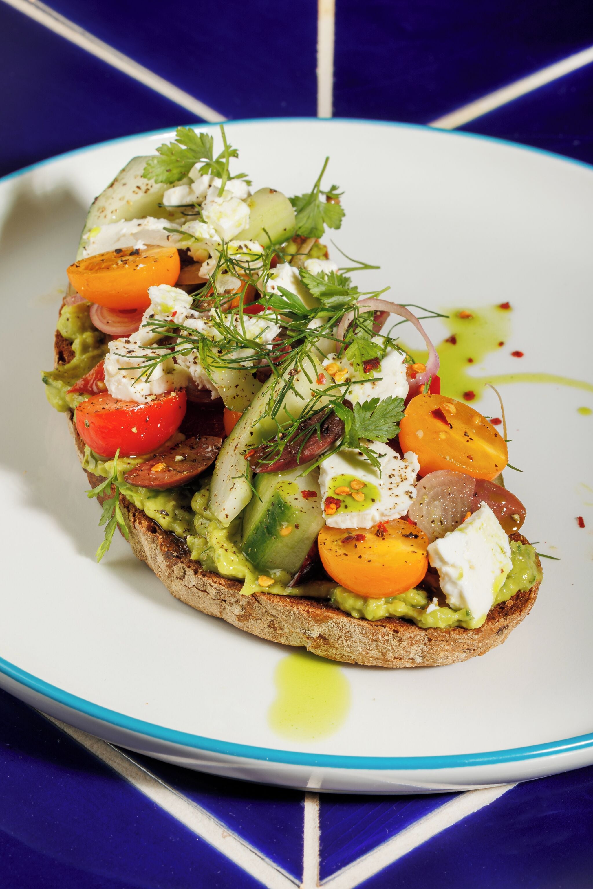 Un sándwich con diferentes ingredientes sobre un plato blanco con borde azul.
