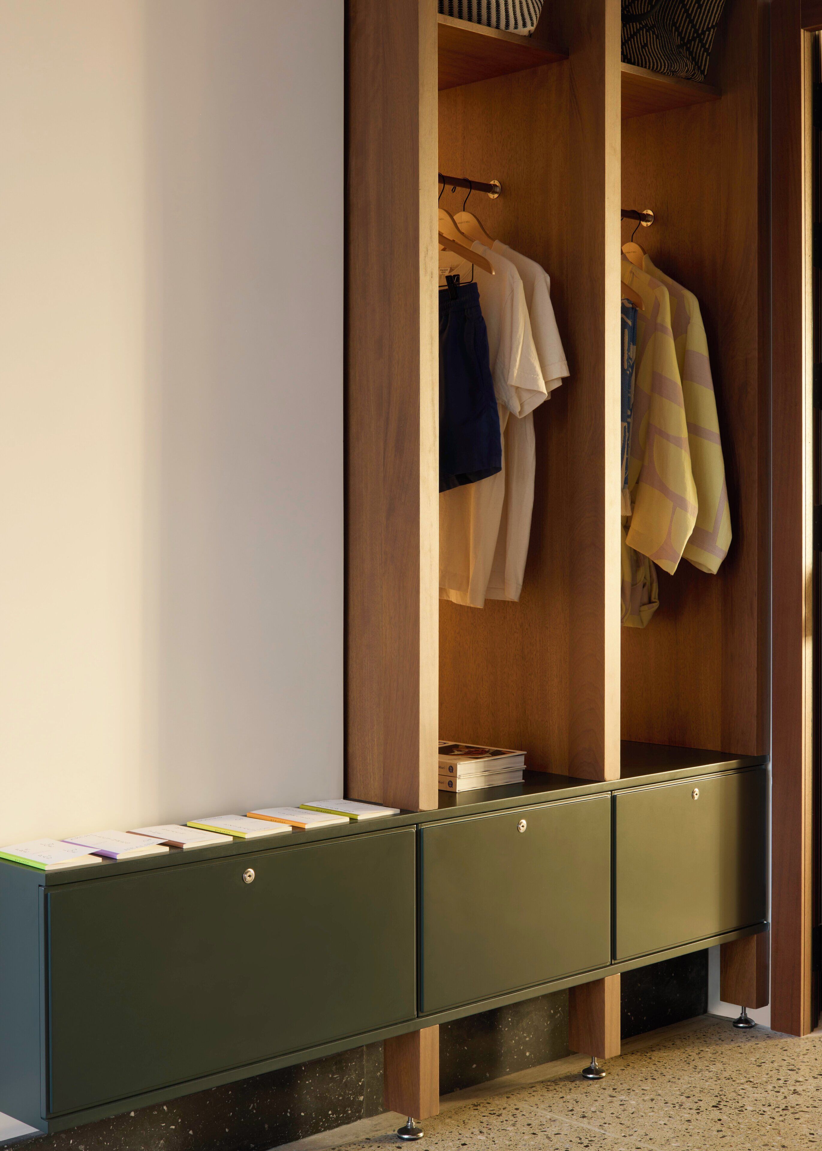 Un dressing avec des portes en bois, une armoire de rangement verte et des vêtements suspendus.