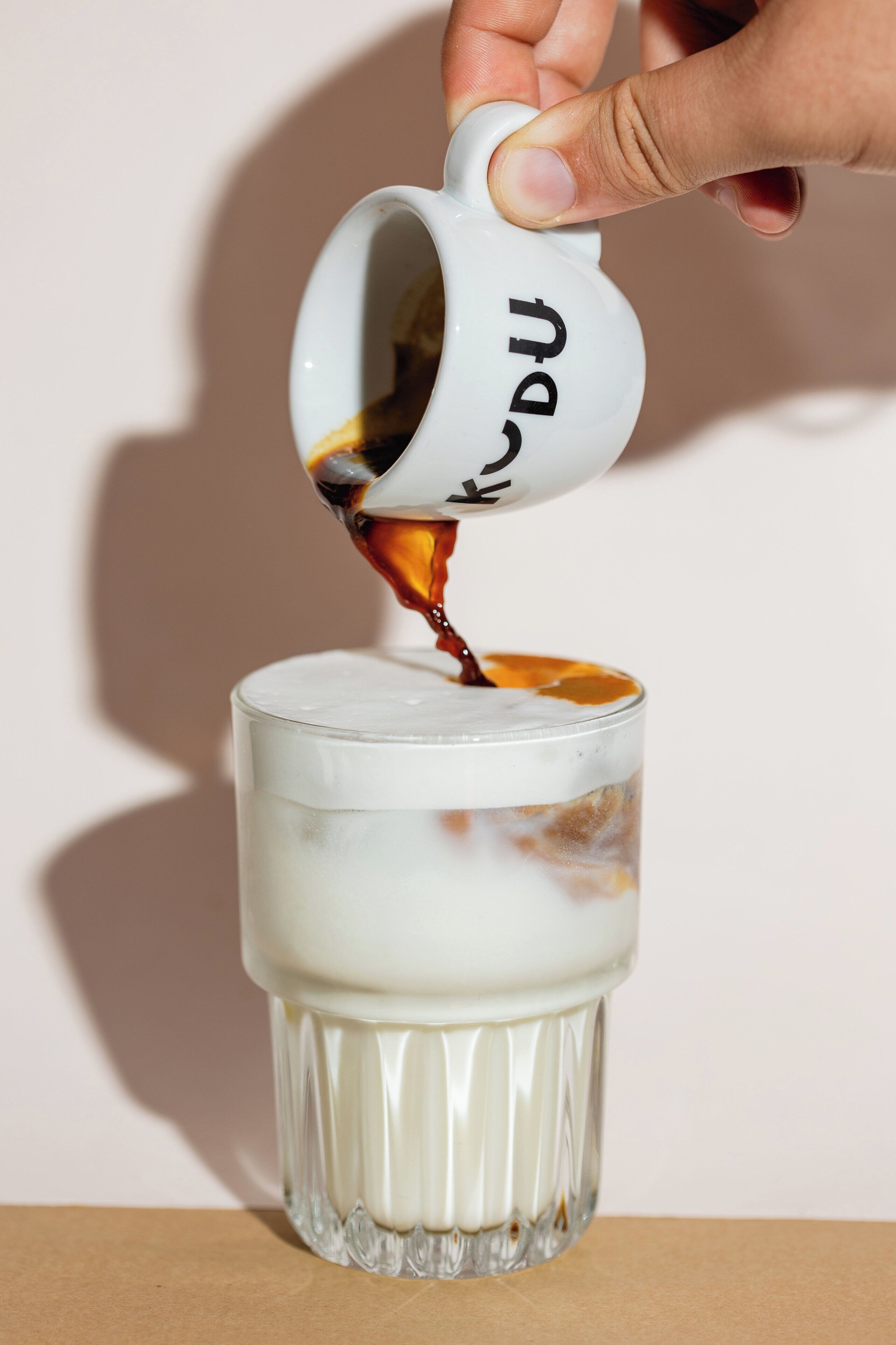 A hand pouring coffee into a glass.
