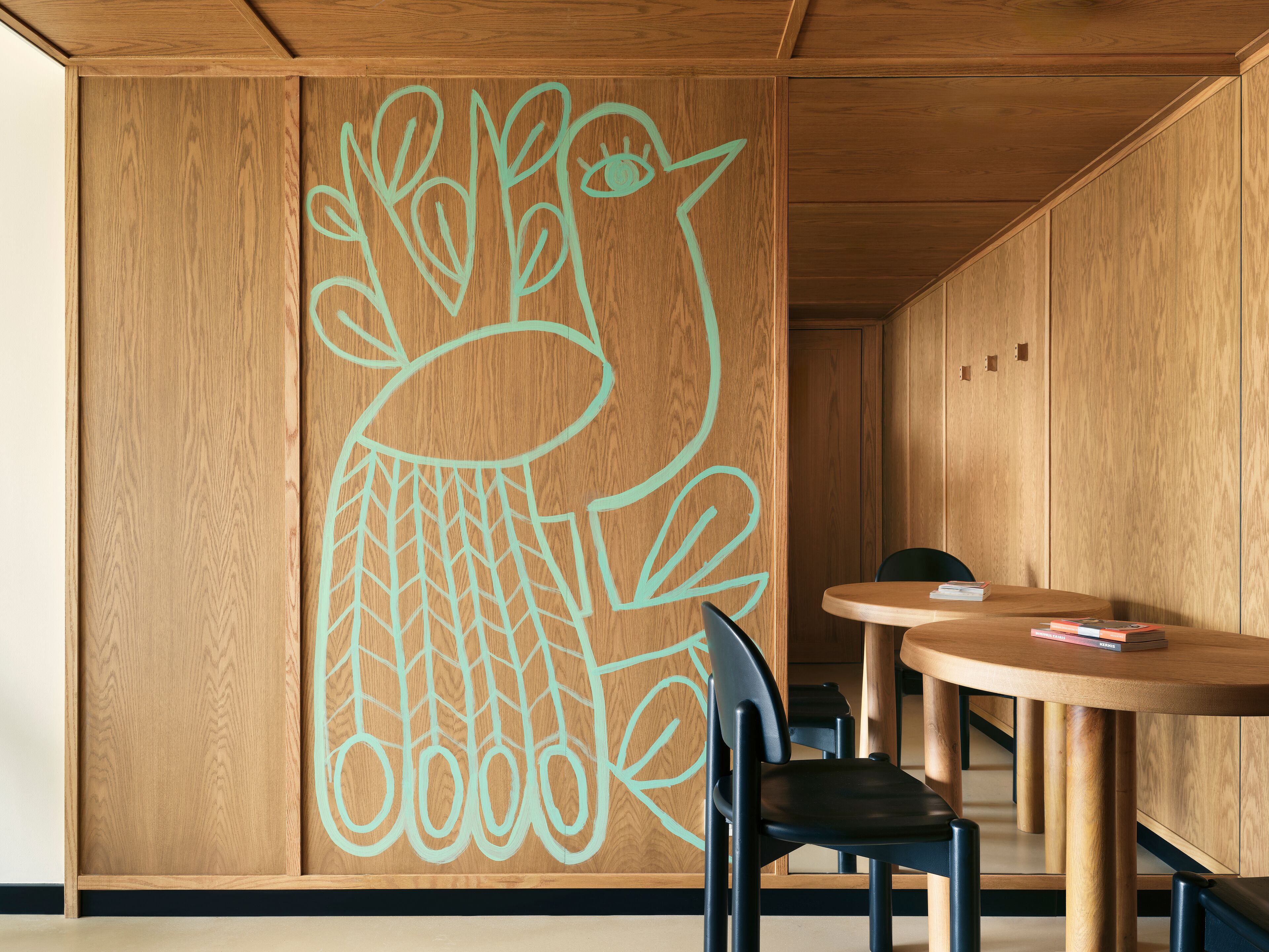 Un interior de madera con un mural grande en la pared, una mesa redonda de madera y una silla negra.