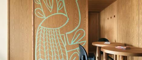 Un interior de madera con un mural grande en la pared, una mesa redonda de madera y una silla negra.