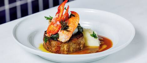 Une assiette blanche sur laquelle on trouve une queue de homard, un morceau de viande et quelques légumes verts.