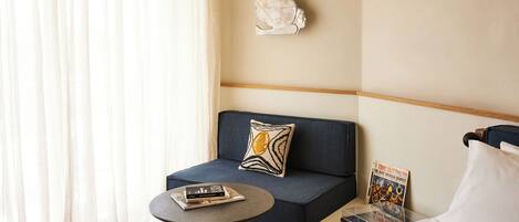 A hotel room with a sofa, a small round table, a bed, and a window with curtains.