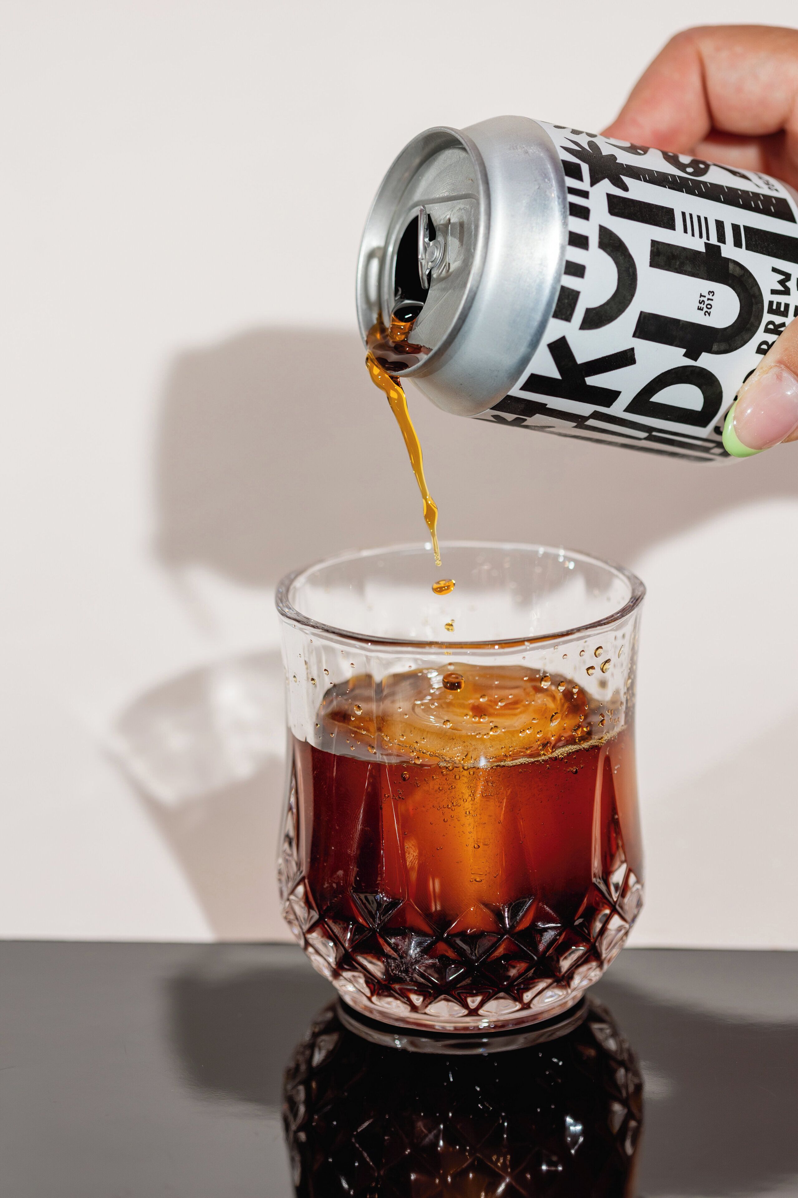 A hand pouring a beverage from a can into a glass.