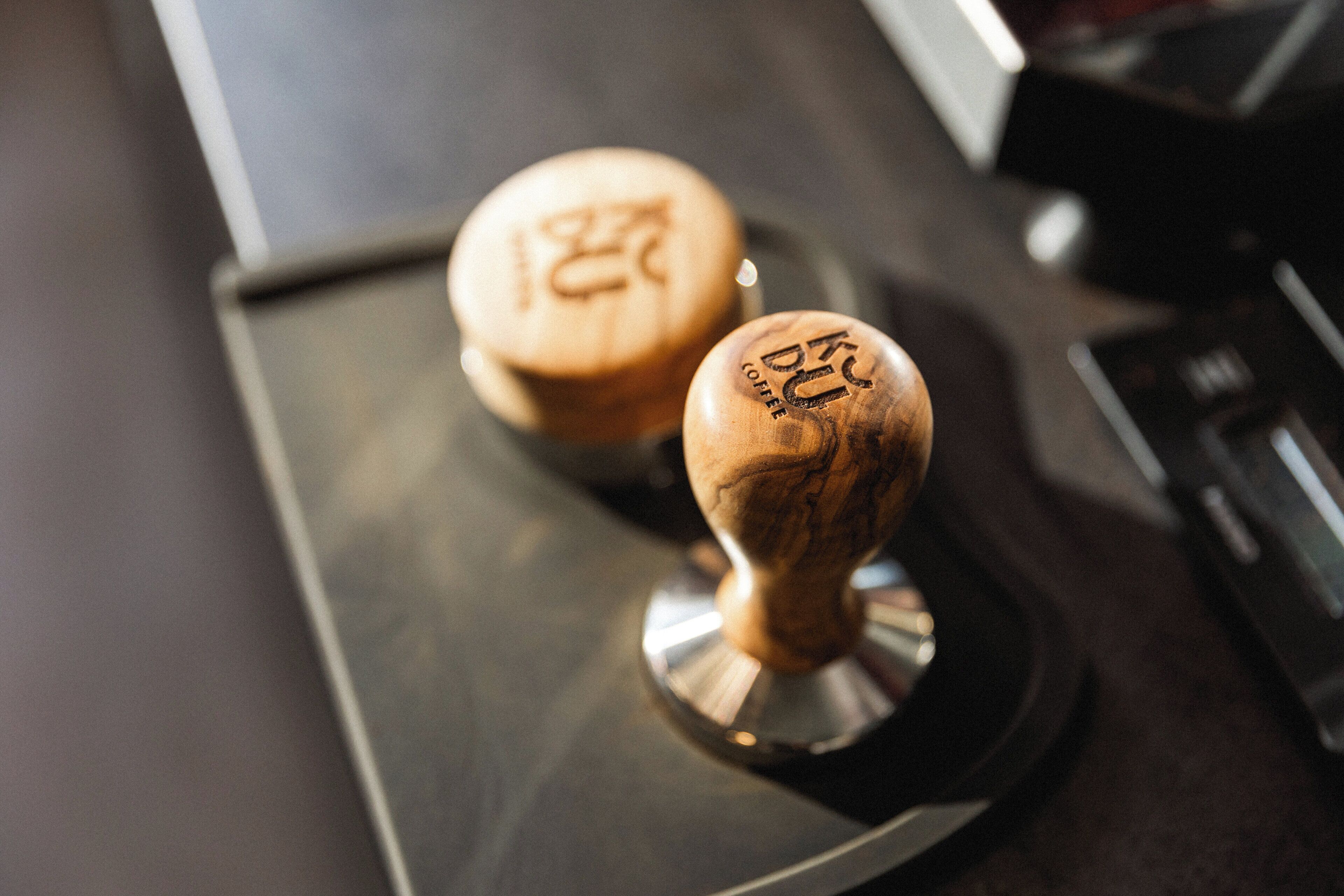 Two wooden coffee press handles with embossed text on a dark countertop.