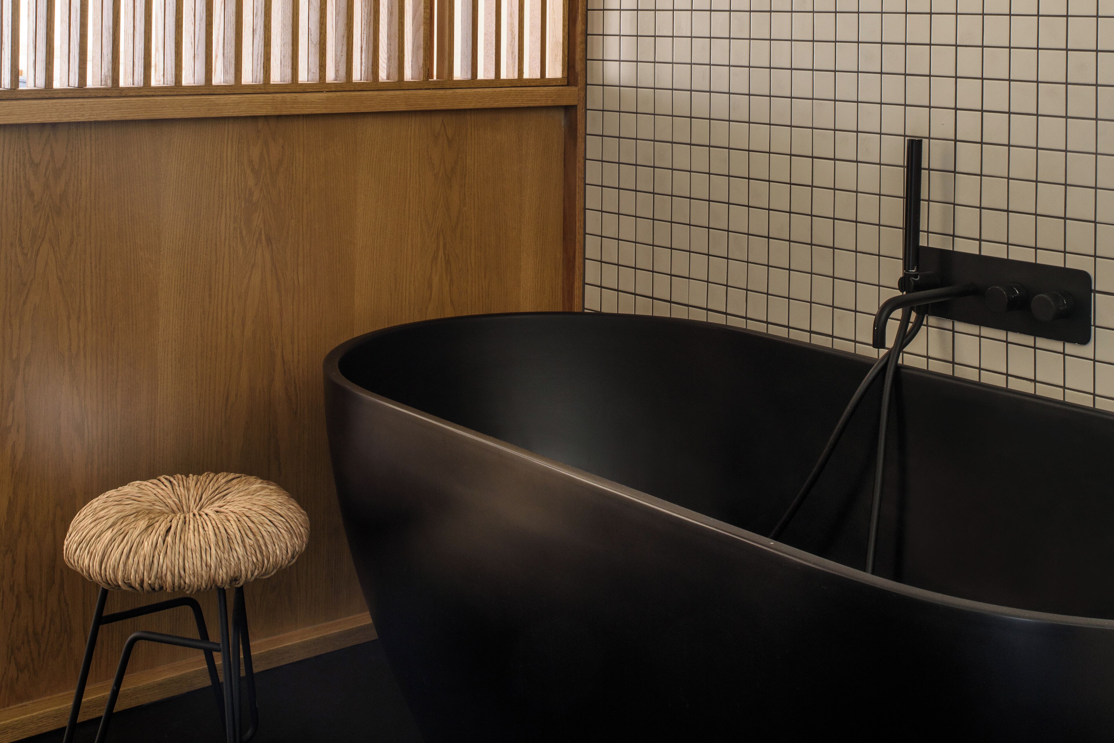 Un bagno moderno con una grande vasca da bagno nera, un pannello di legno a parete e un piccolo sgabello.