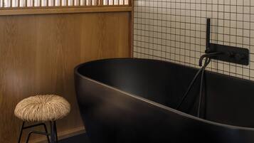 Un bagno moderno con una grande vasca da bagno nera, un pannello di legno a parete e un piccolo sgabello.