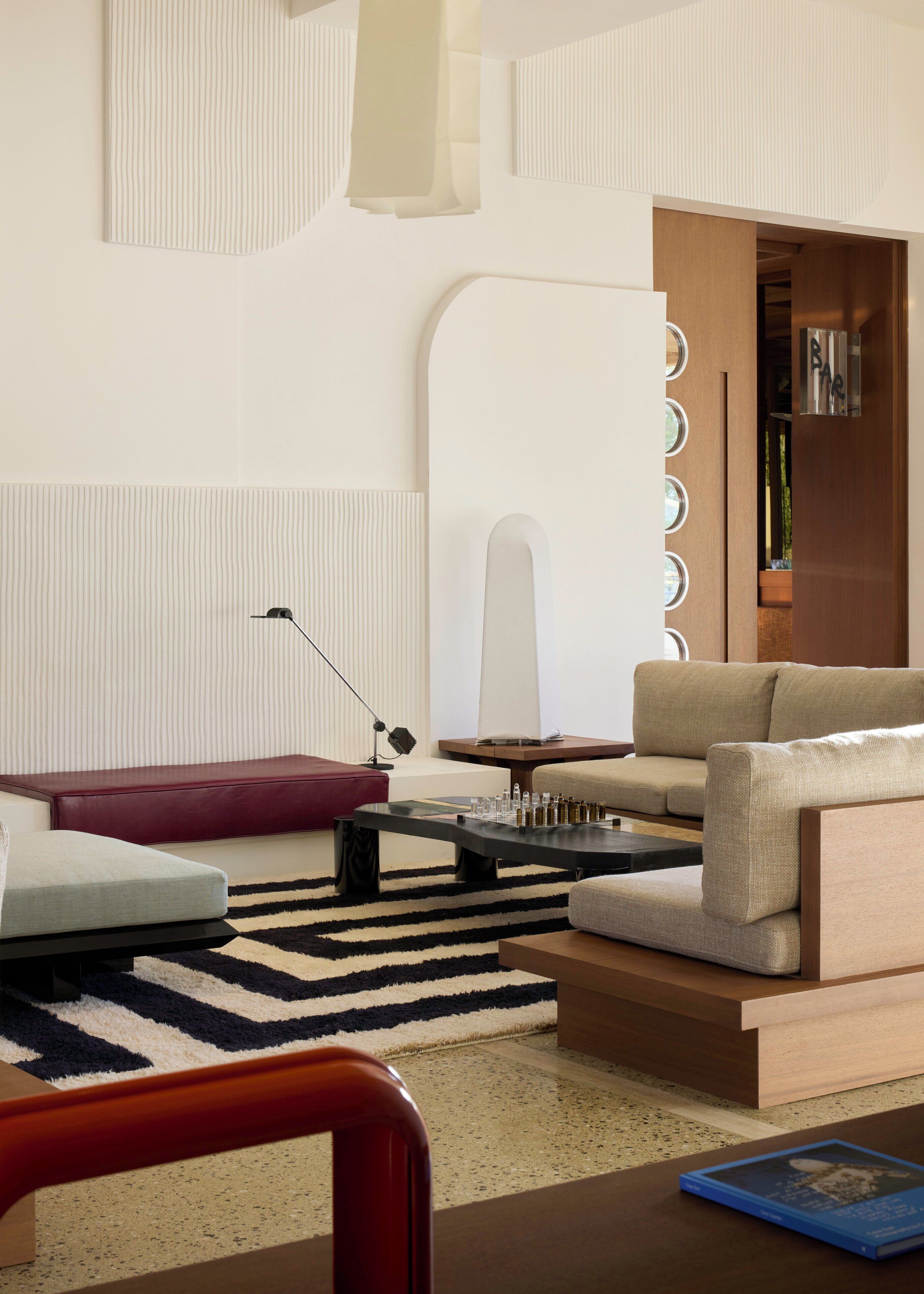 A modern living room with a sofa, a coffee table, and a red chair. There is a bookshelf with books and a lamp.