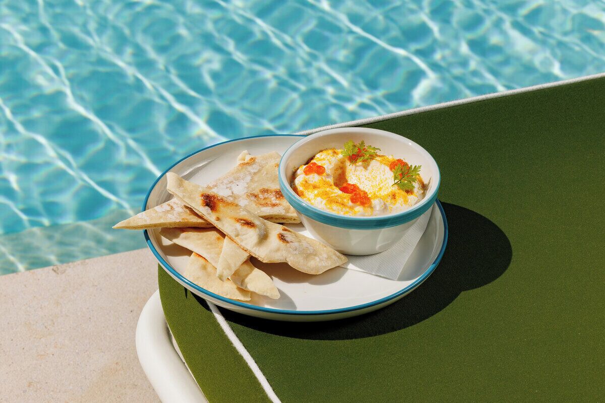 A plate with flatbread and a bowl of dip by a poolside.