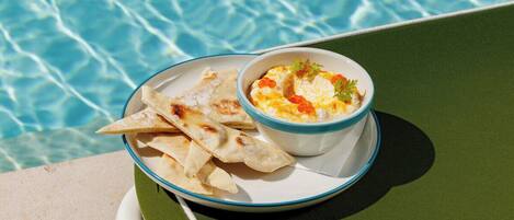 A plate with flatbread and a bowl of dip by a poolside.