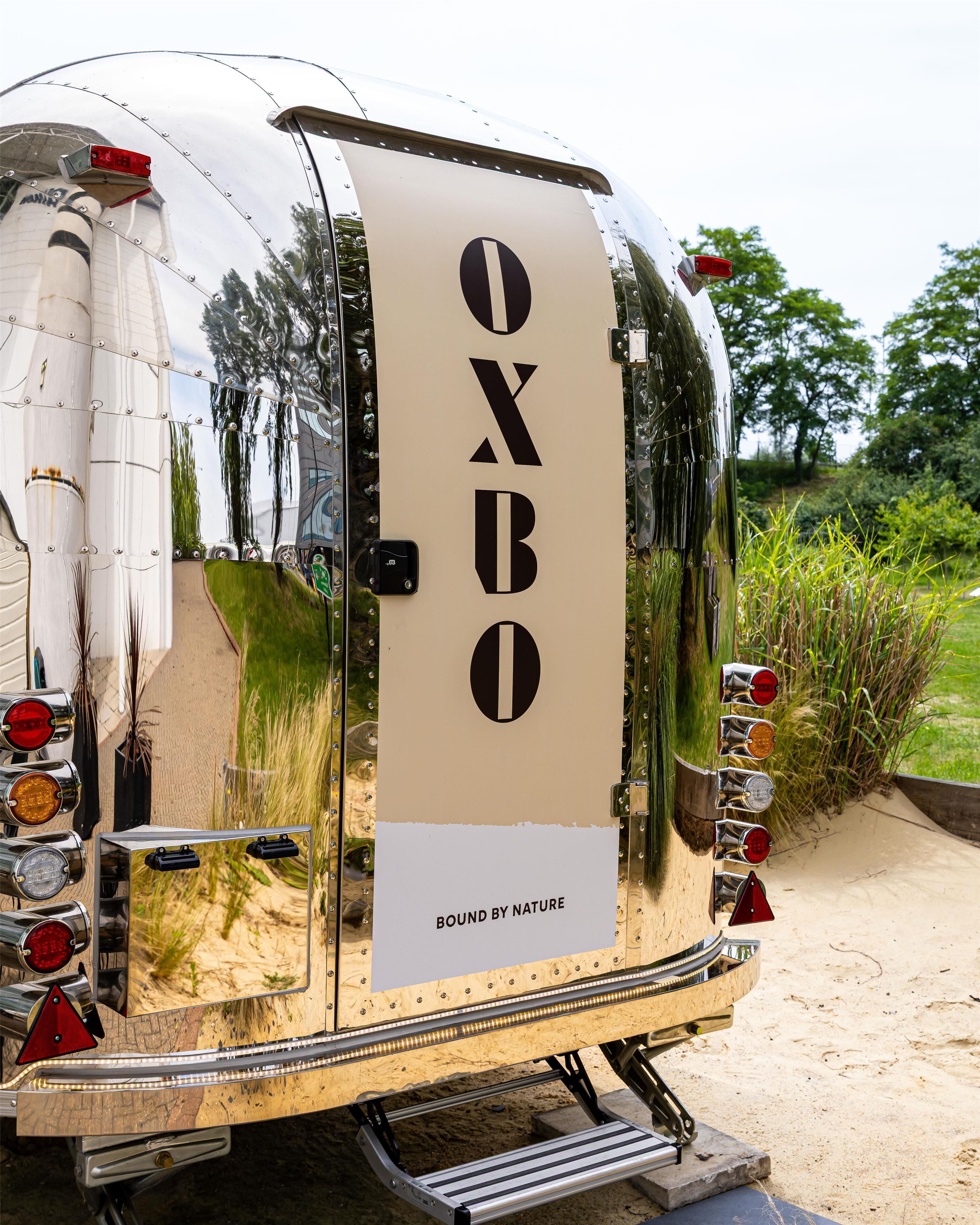 A vintage camper with 'OXBO' branding and 'BOUND BY NATURE' text on the side.