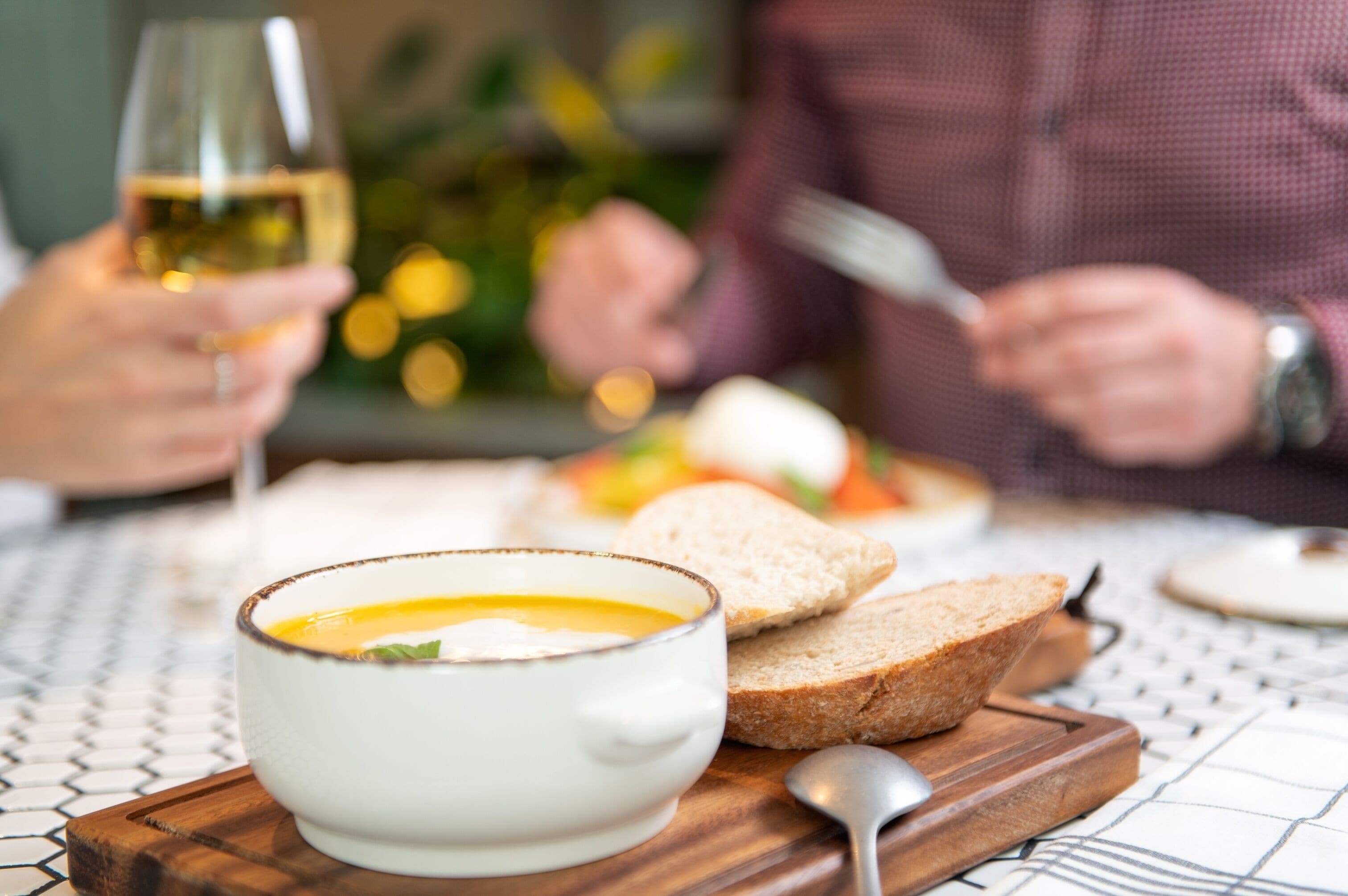 Una mesa de comedor con un tazón de sopa, rebanadas de pan y una copa de vino.