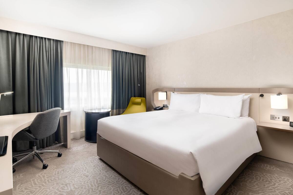 Hotellihuone, jossa on suuri sänky, työpöytä, tuoli, yöpöytä ja lamppu.