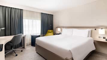 A hotel room with a large bed, a desk, a chair, a bedside table, and a lamp.