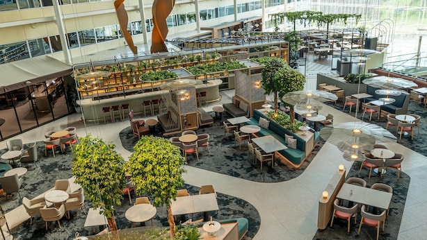A spacious indoor area with multiple seating arrangements, including tables and chairs, surrounded by greenery and modern lighting fixtures. - Hilton London Heathrow Airport Hotel (Hounslow)