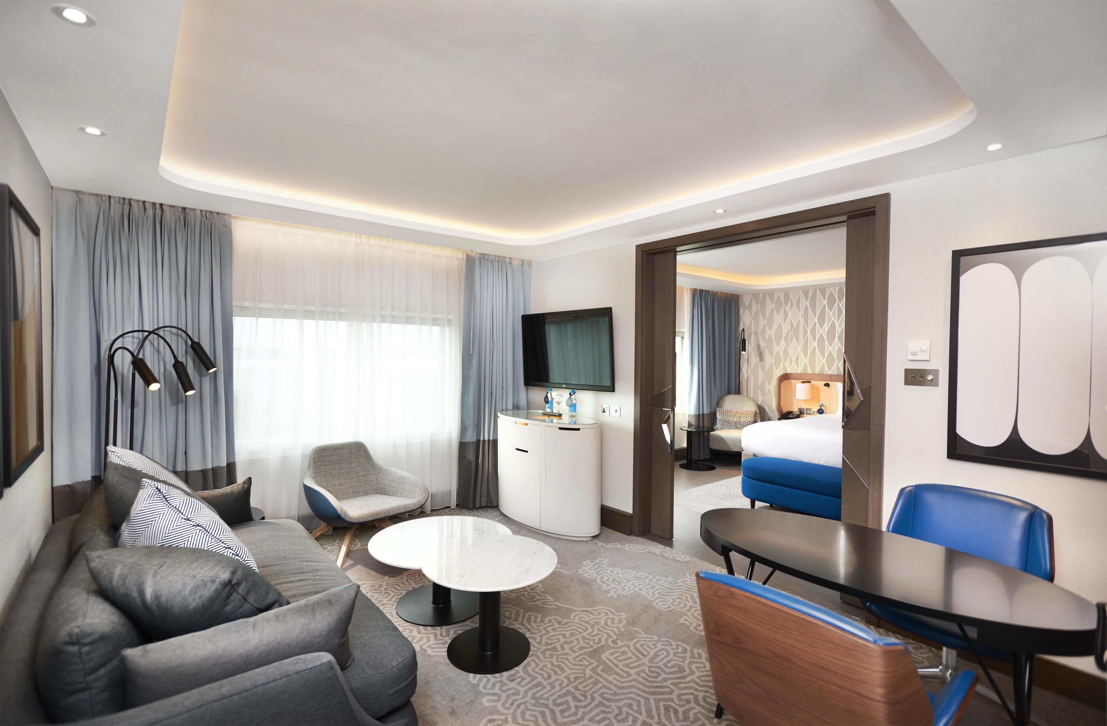 Una habitación de hotel moderna con sofá, sillón, mesa de comedor y cama.