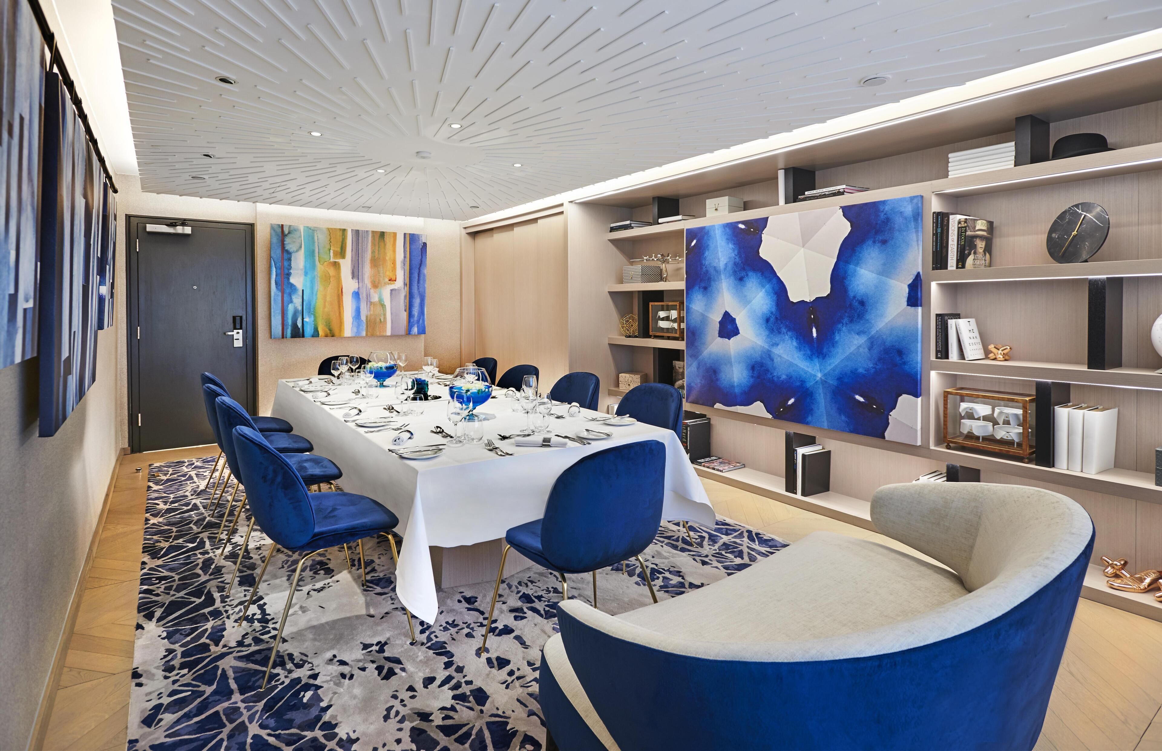 A dining area with a table set for six, blue chairs, and abstract art on the walls.