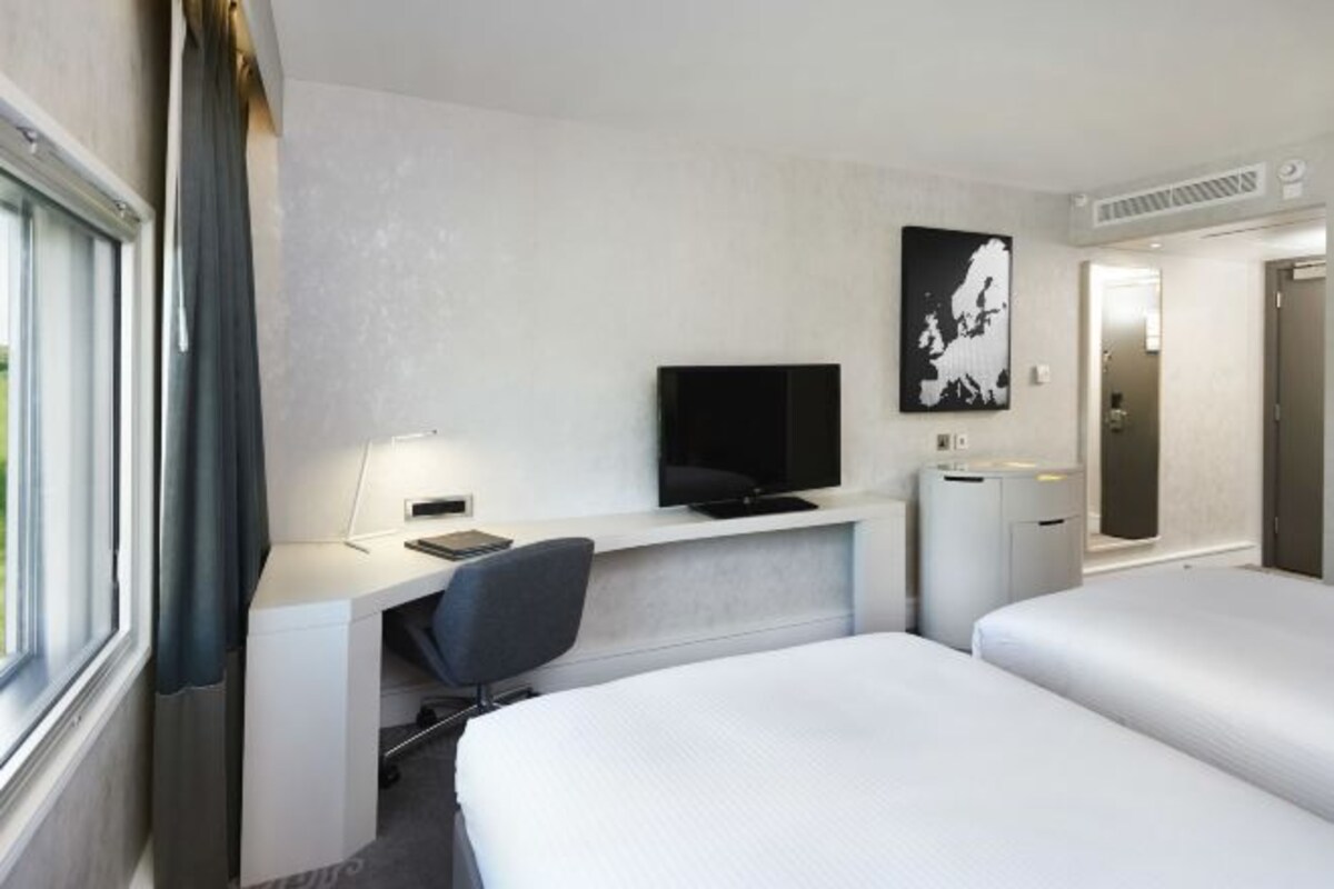 Une chambre d’hôtel comprenant un lit, un bureau avec une chaise, une télévision et un petit meuble de rangement.