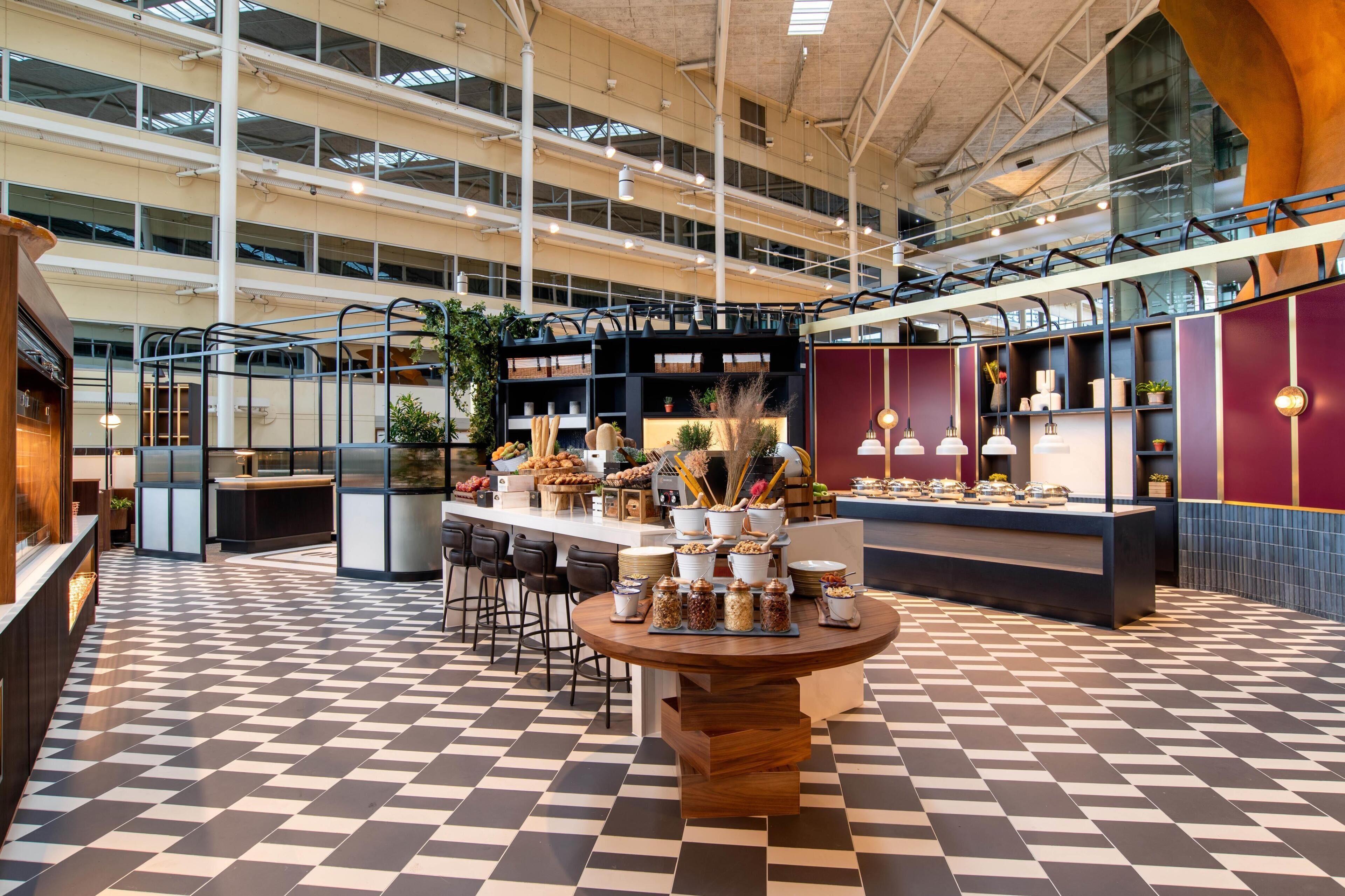 A spacious indoor area with a checkered floor, multiple seating arrangements, and a central table with food items.