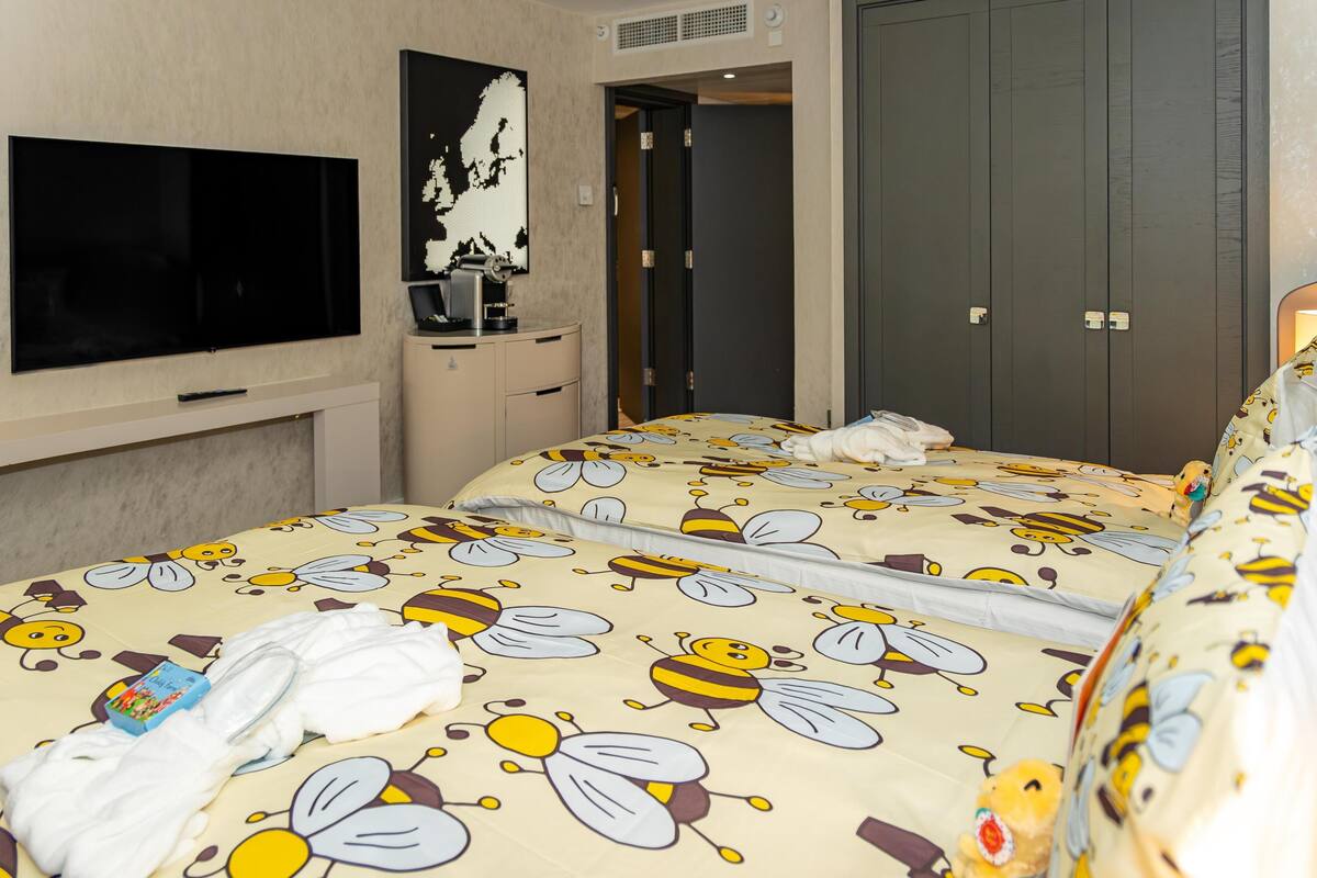 Hotellihuone, jossa on mehiläiskuviollinen sängynpeite, taulutelevisio, kahvinkeitin ja vaatekaappi.