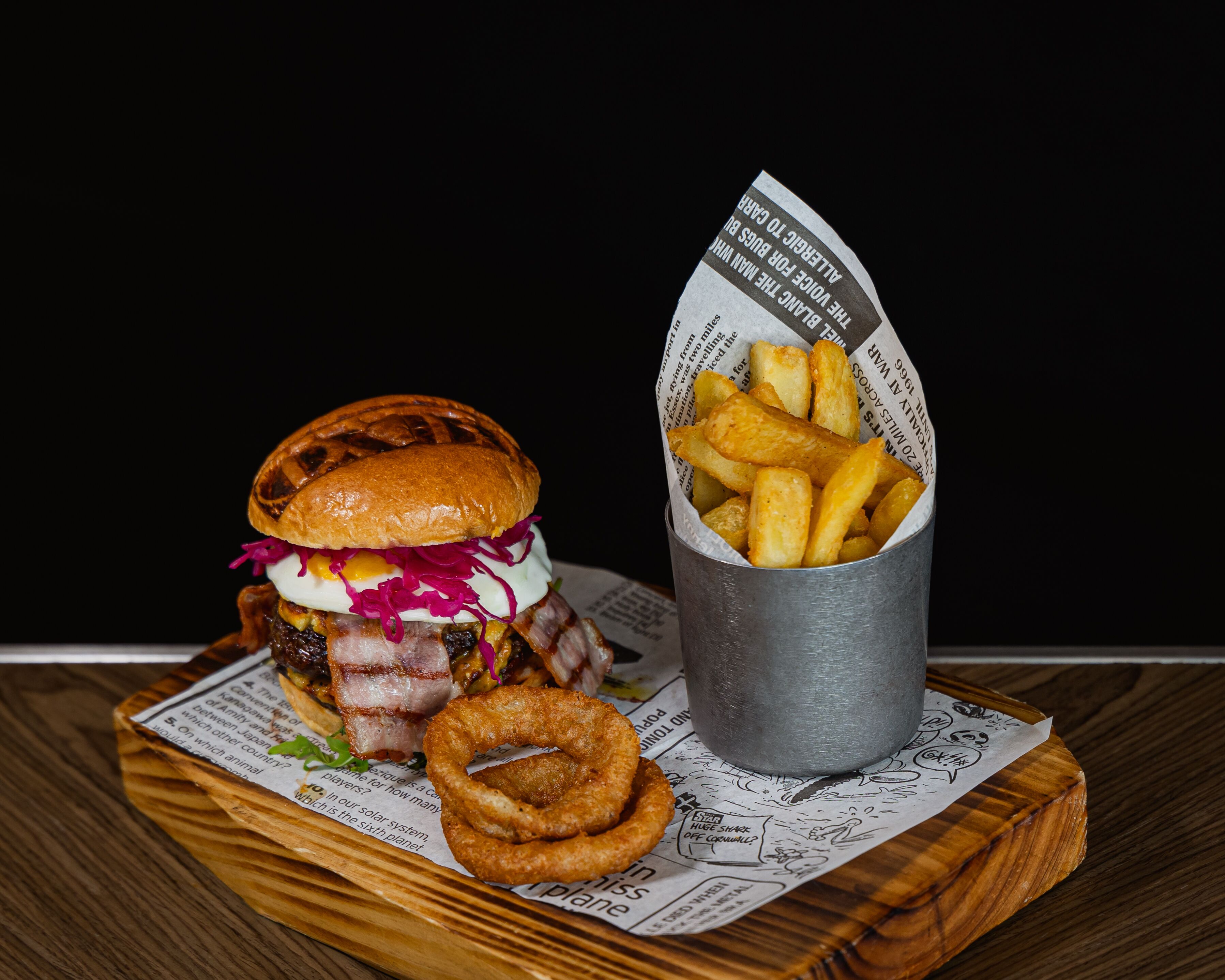 Burger med pommes frites og løgringe på en tr æplade.