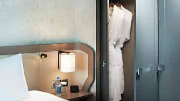 A hotel room with a bed, a bedside table with a lamp, a bottle, and a clock.
