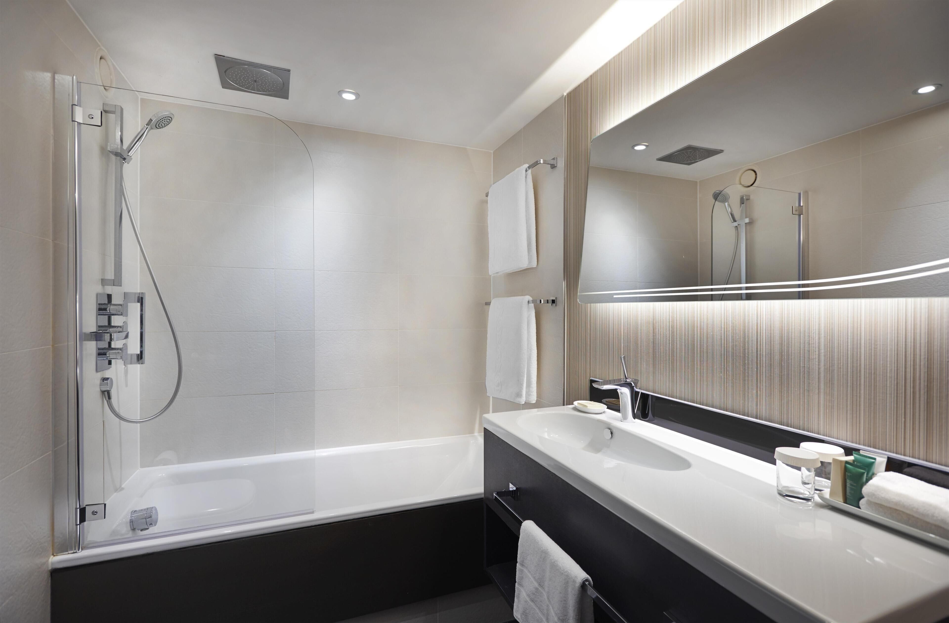 A modern bathroom with a glass-enclosed shower, a large mirror, and a vanity with a sink and towel rack.