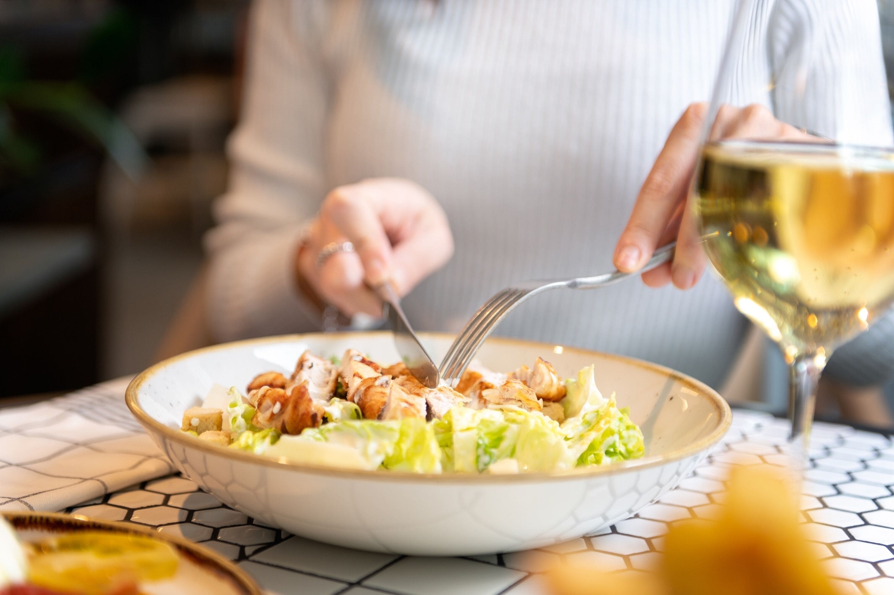 A person dining at a table with a bowl of salad and a glass of white wine.