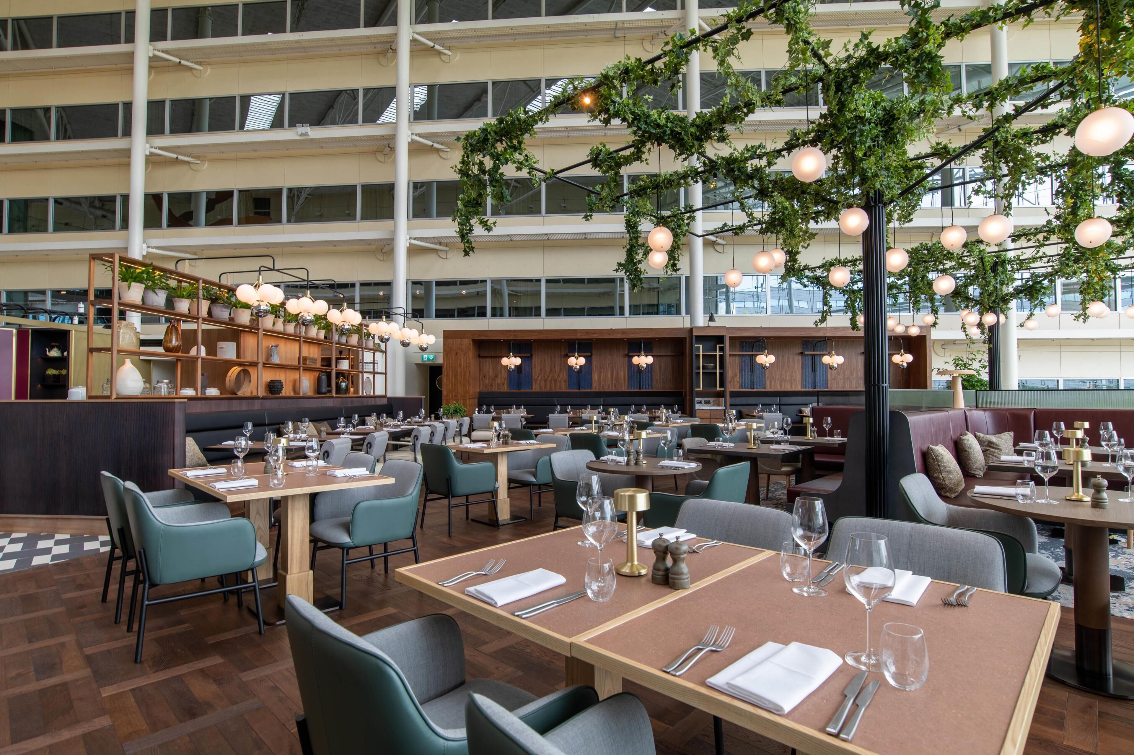 A spacious restaurant with multiple dining areas, a central plant display, and hanging spherical lights.