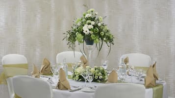 A table set for a formal event with a floral centerpiece, white tablecloth, and chairs with green sashes.