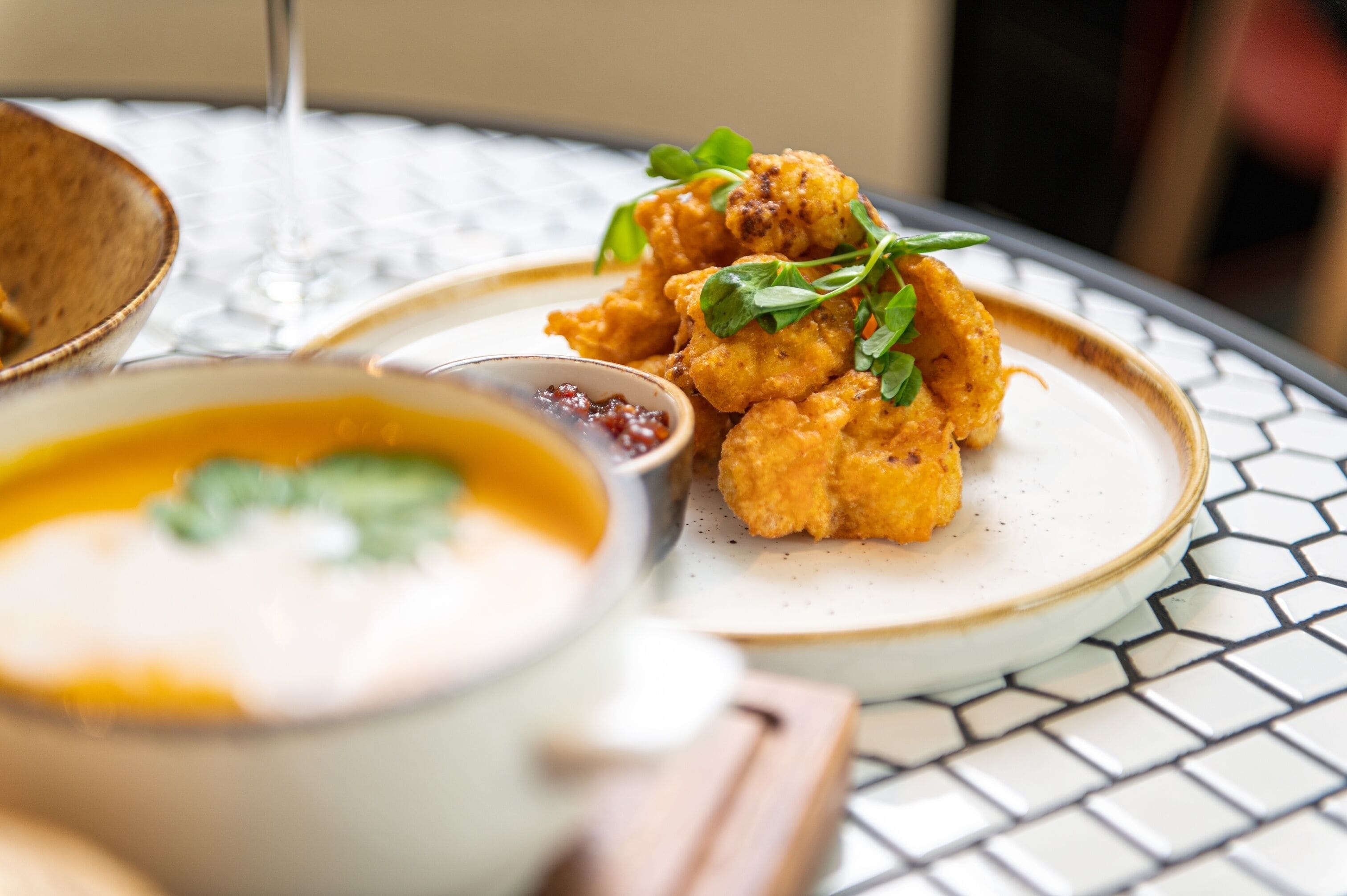 A table with a plate of fried food garnished with greens, a bowl of soup, and a glass of water.