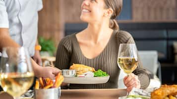 A dining table with a plate of food, a glass of white wine, and a person holding a fork.