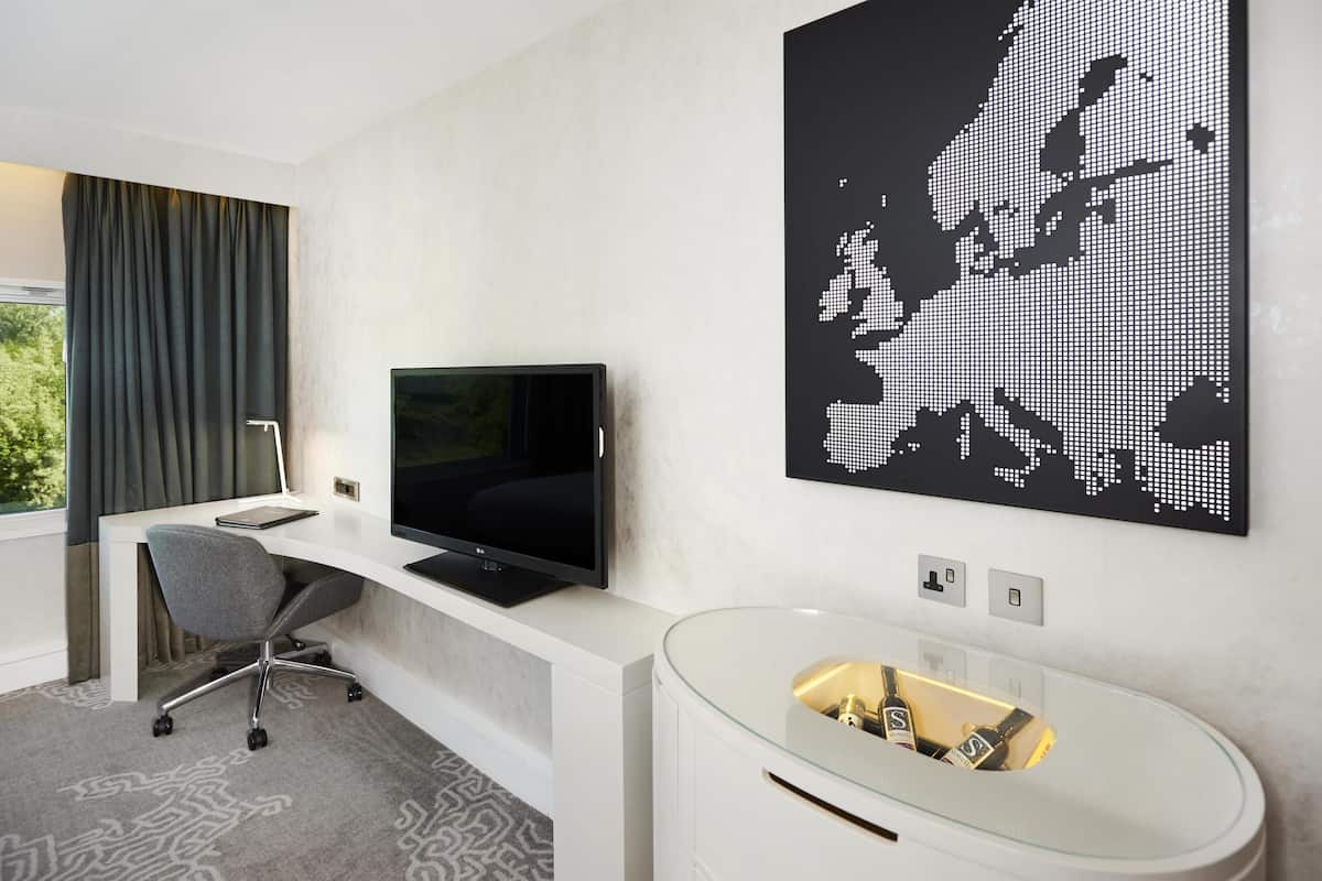 Moderni hotellihuone, jossa on työpöytä, televisio ja suuri maailmankartta, joka on koristeltu seinälle taideteokseksi.